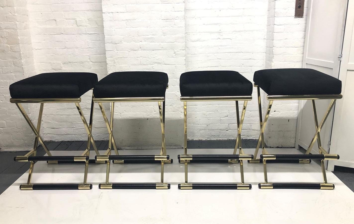 Set of four 1980s velvet and brass finish bar stools. The frames are brass finish and the footrests and bases are covered in black vinyl. The cushions of the bar stools are black velvet.
