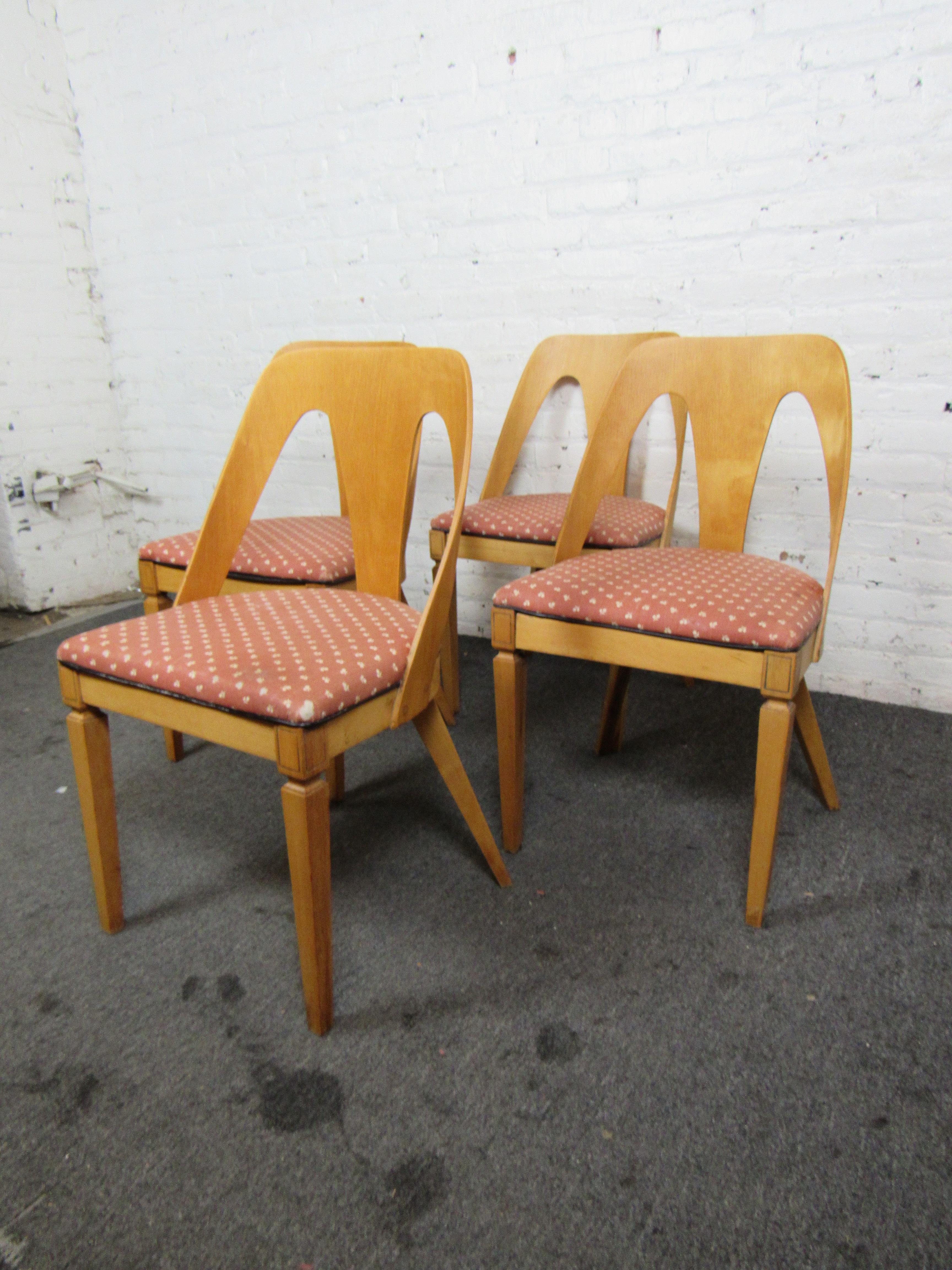This set of four vintage dining chairs pair a light wood grain with warm red upholstery on cushioned seats. A minimal Mid-Century design for the chair's backs make this set a beautiful way to add timeless style to a dining room. 

Please confirm
