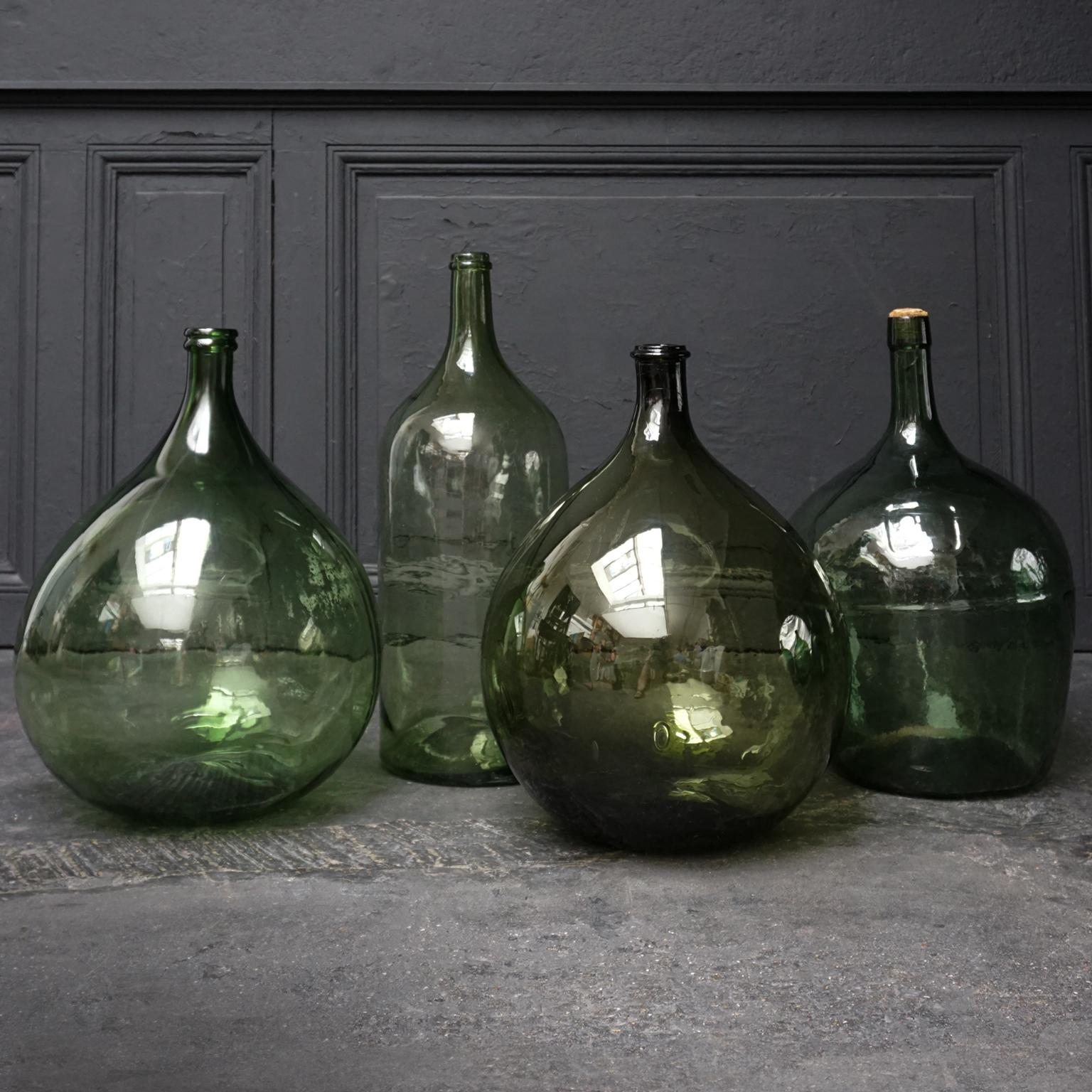 Very decorative set of 4 old green blown and pressed glass bottles also know as Demijohn, Lady Jeanne, Dame Jeanne or Carboy.
Made and used somewhere between early 20th century and 1960s. 

The two bulbous ones of them have a capacity of 25