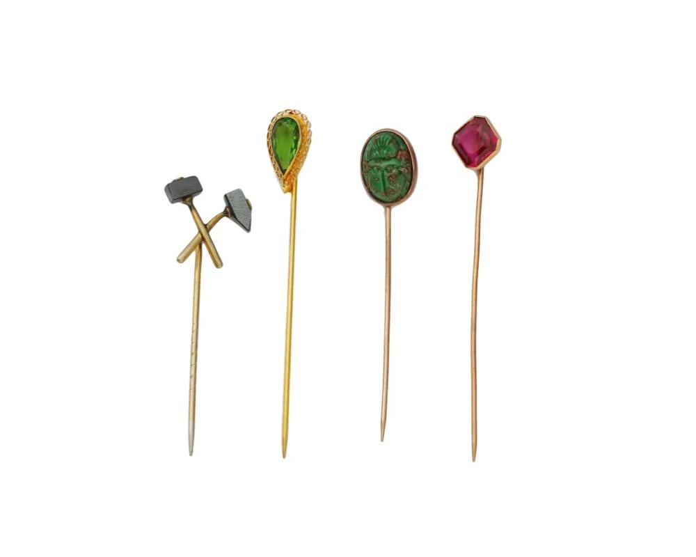 Un ensemble de quatre pin's vintage, chacun présentant un design unique. La première épingle est ornée de deux marteaux croisés. La seconde est une épingle en or sertie d'une pierre précieuse verte à facettes, entourée d'un cadre ajouré et marquée