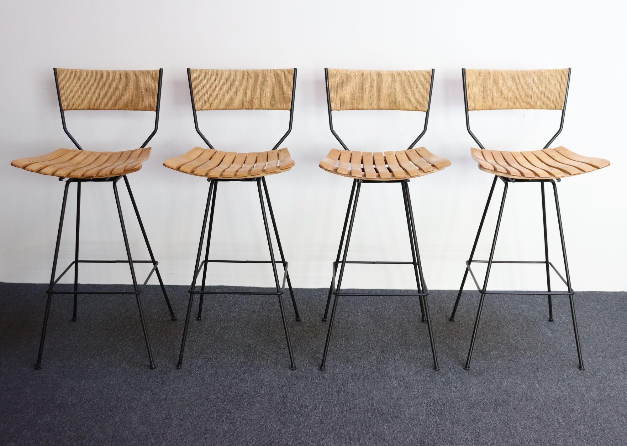 Set of four Arthur Umanoff for Shaver Howard bar stools composed of wrought iron frames with birch-slatted seats (ca. 1950s, USA).
Modernist, rectangular rush back adds a striking contrast to an otherwise modest form.
Swivel seat allows for full 360
