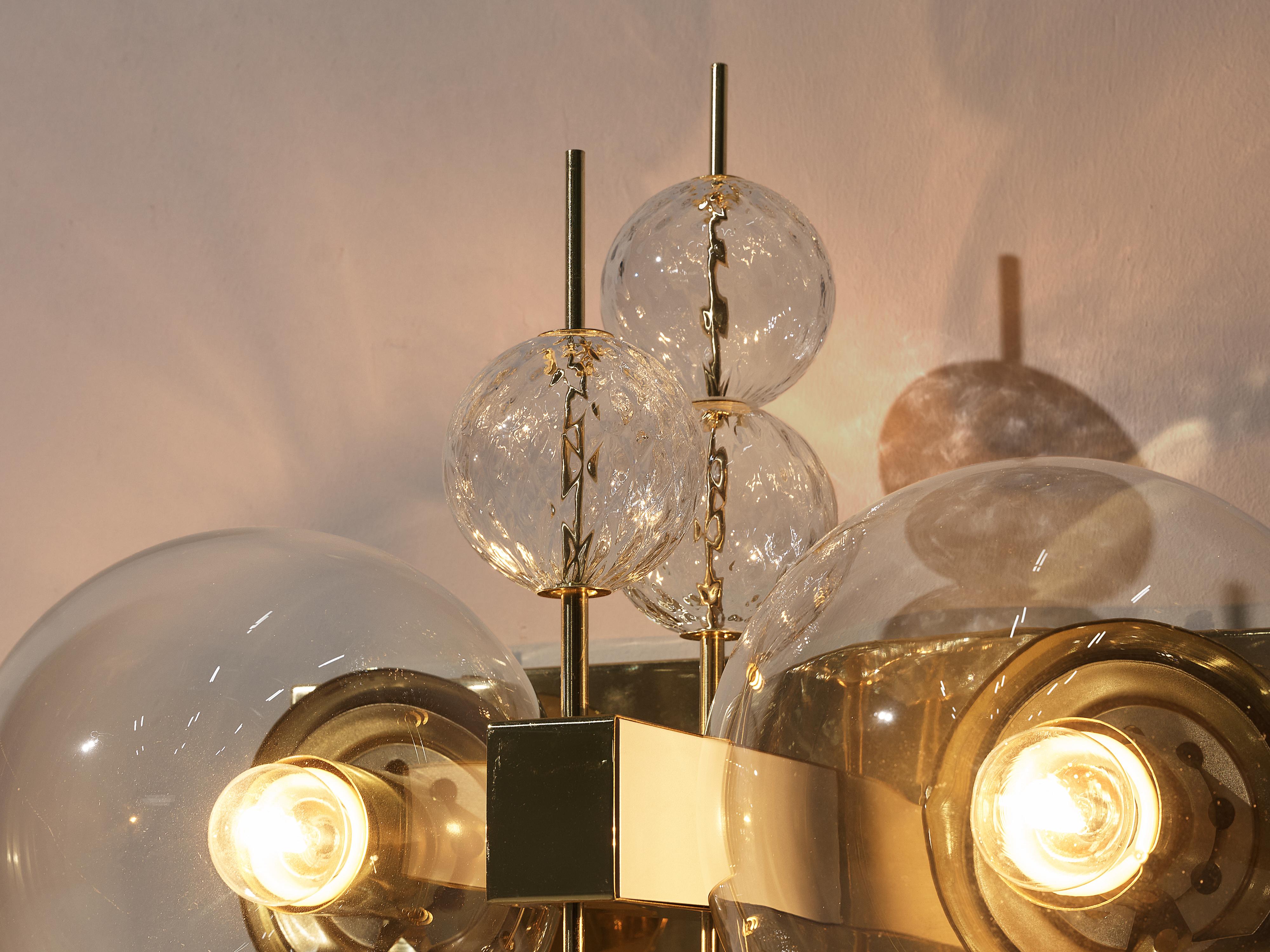 Wall lights, glass and brass, Europe, 1970s.

Captivating wall lights adorned with intricate brass details and delicate glass elements. Two light points gracefully emerge, casting a soft glow that dances through the structured glass globes. Each