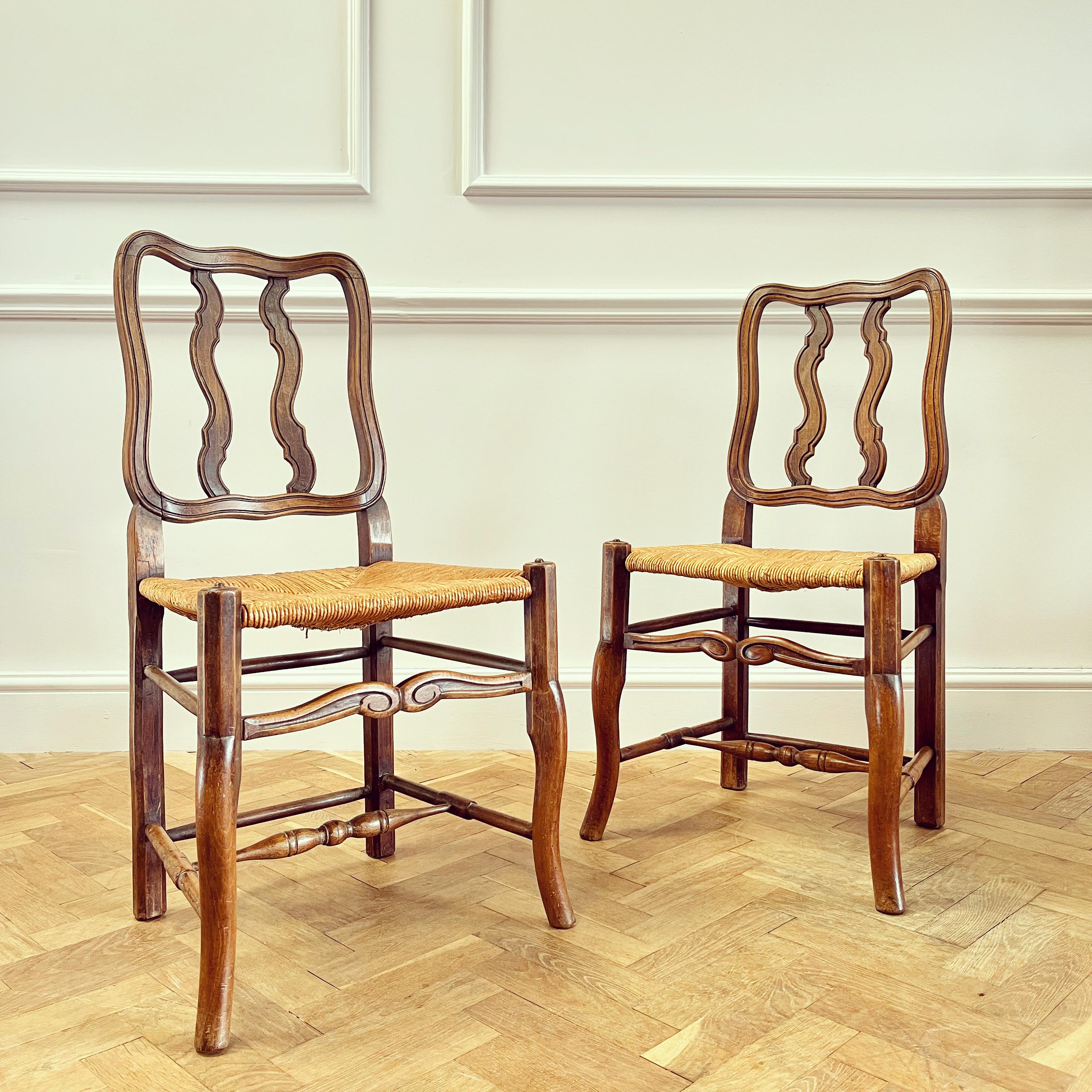 A very elegant set of fourteen French oak vernacular dining chairs, the backs wavy with shaped and reeded slats, with wide rush seats and cabriole front legs with concentric circles to top and turned supports beneath.

French , Early Twentieth