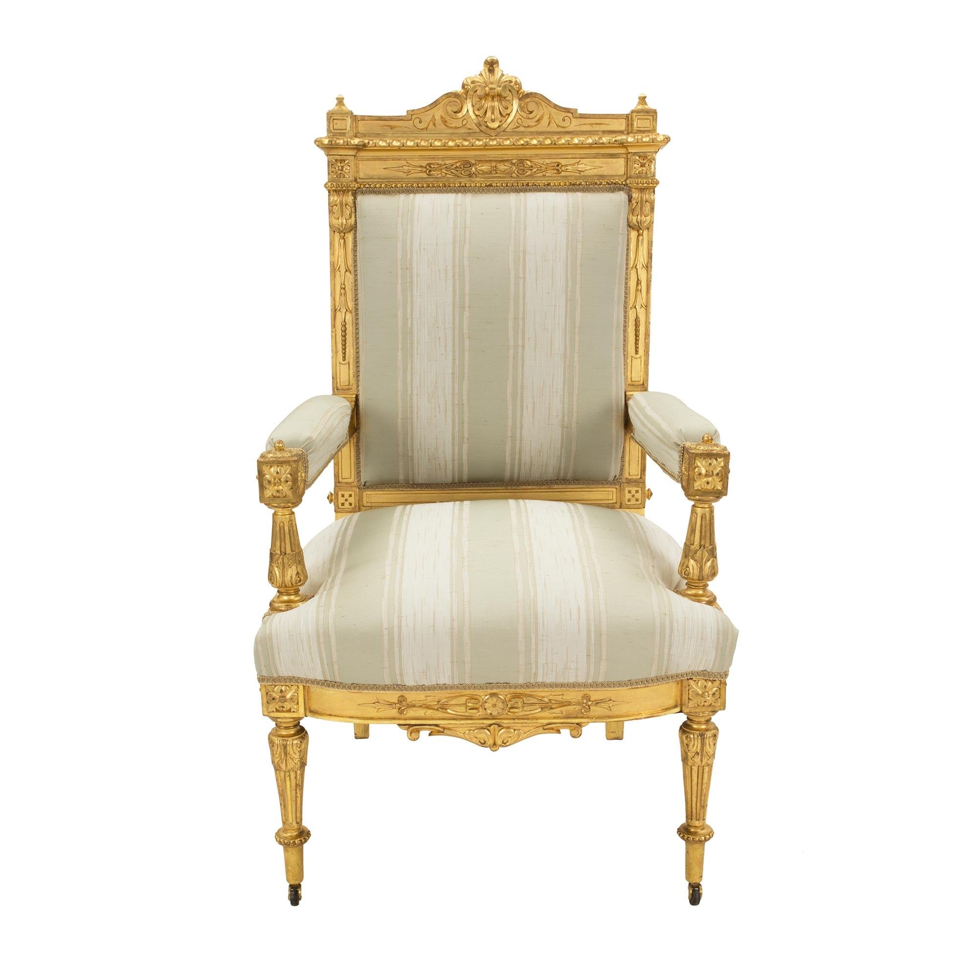 A stunning and complete set of fourteen French 19th century Louis XVI st. giltwood dining chairs. This large set comprises of two armchairs and twelve side chairs. Each chair is raised by their original casters below finely carved circular tapered