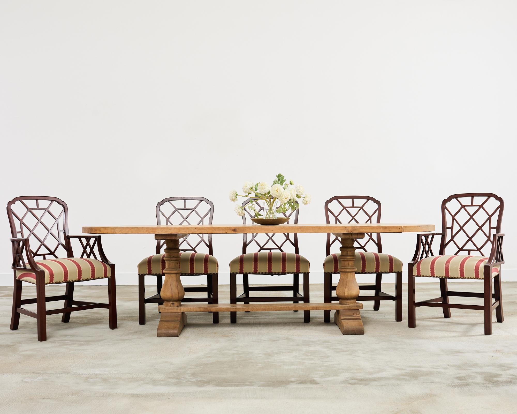 Monumental set of fourteen stately English dining chairs made in the George III taste. The opulent chairs feature a Chinese Chippendale style with carved open fretwork designs on the back and arms also known as cockpen chairs. The grand set consists