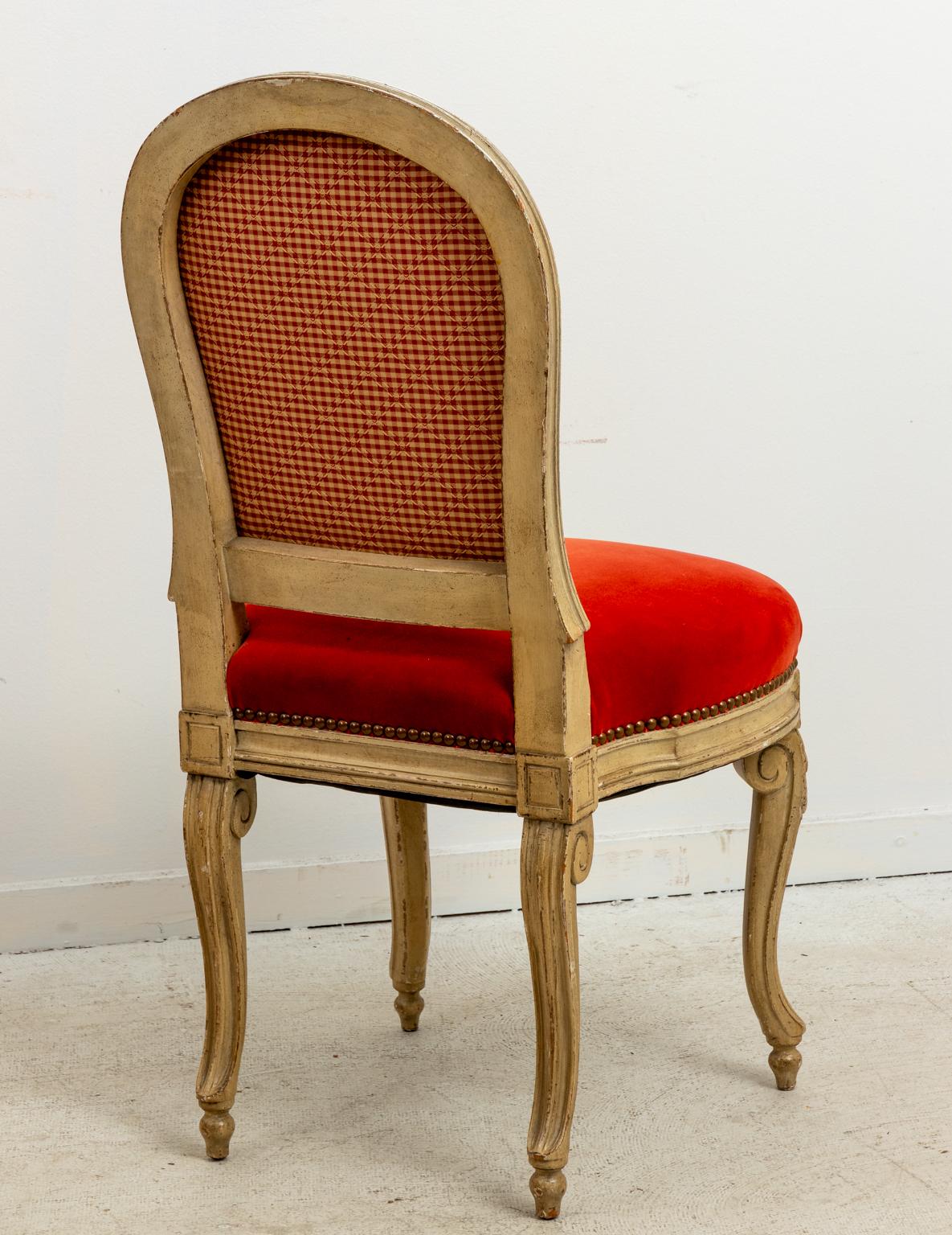 Set of fourteen French dining chairs upholstered in orange velvet with distressed finish, circa 1920s. The chairs also feature metal nail head trim and scrolled legs. Please note of wear consistent with age including finish loss and paint loss. One