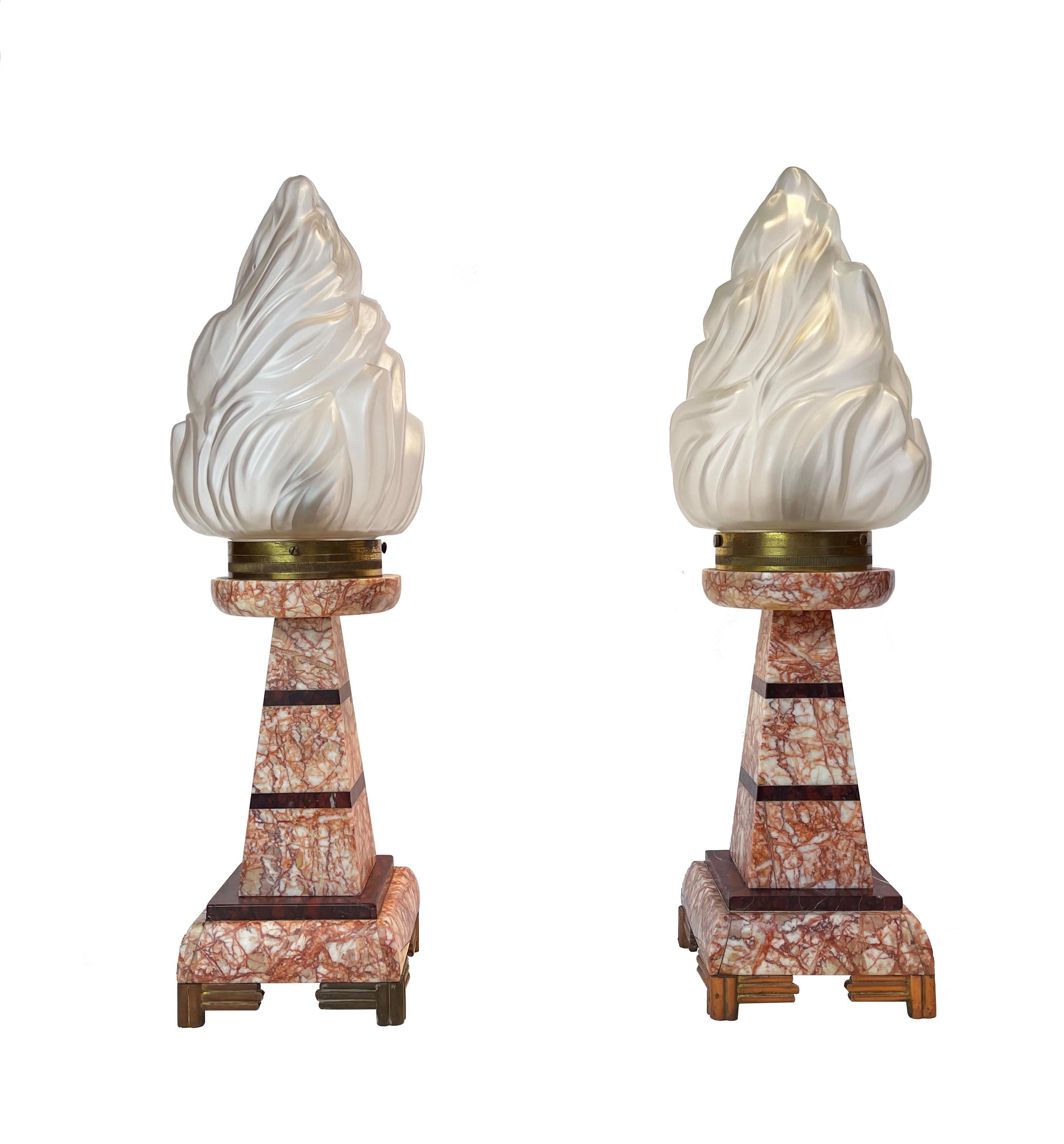 Ausdrucksstarkes und in der Tat ungewöhnliches Set aus zwei französischen Art-Déco-Tischlampen mit einem Hauch von Empire-Stil aus den 1930er Jahren.
Diese besondere Art von Fackelscheinwerfern wurde auf der Pariser Ausstellung im Jahr 1855