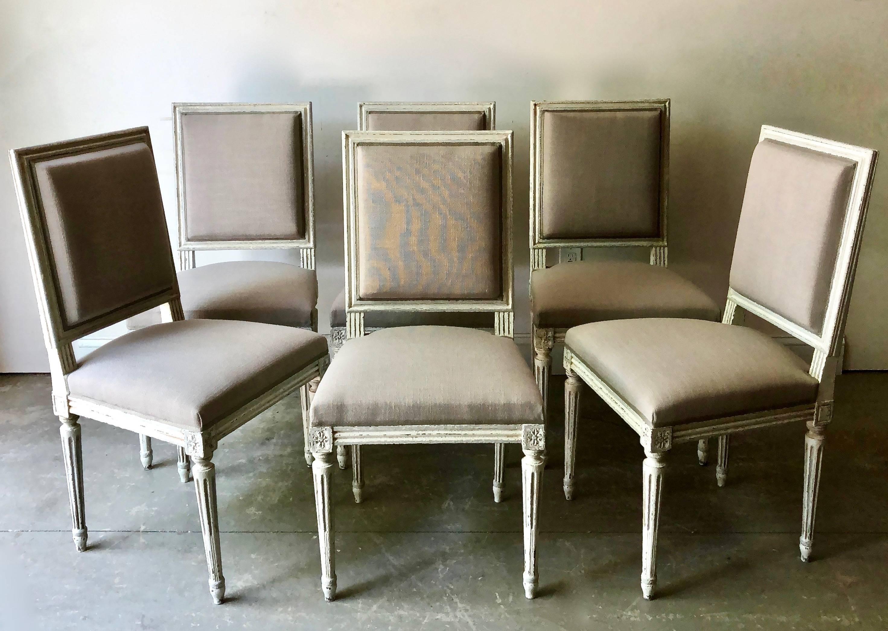 Set of six French Louis XVI style chairs with wood frames in lovely cream-grey-blue painted finish in richly carved frame, fluted leg and cubic blocks decorated with florets. Upholstered in linen and finished with the Classic decorative cimp,