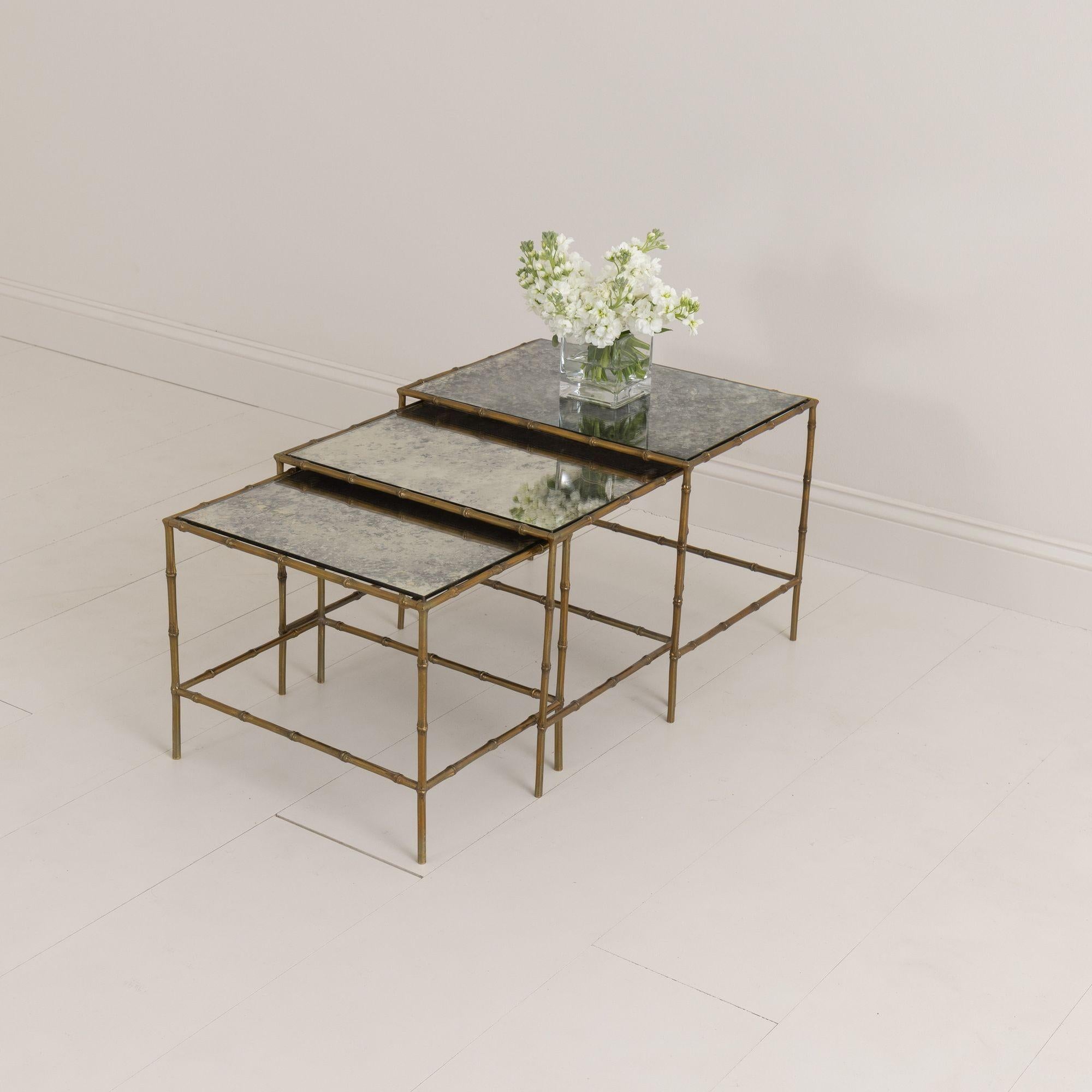 A beautiful set of three nesting tables by French Maison Baguès, created with solid bamboo shaped bronze.  The tops are finished with a mirrored églomisé glass set inside the faux bamboo frames. Circa 1950-60.  The technique of making the églomisé