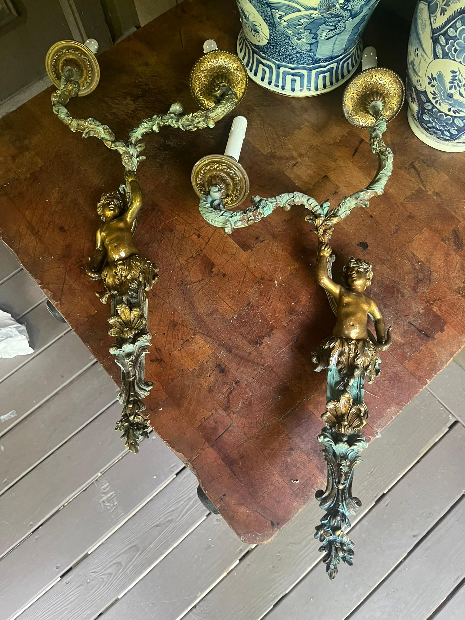 Charmingly distressed bronze sconces with central Bacchus styled figures holding two arms in free form of floral vines , each ending in candle form lights .
The central figures with laurels burnished and resemble gilt ,other areas in green verdigris