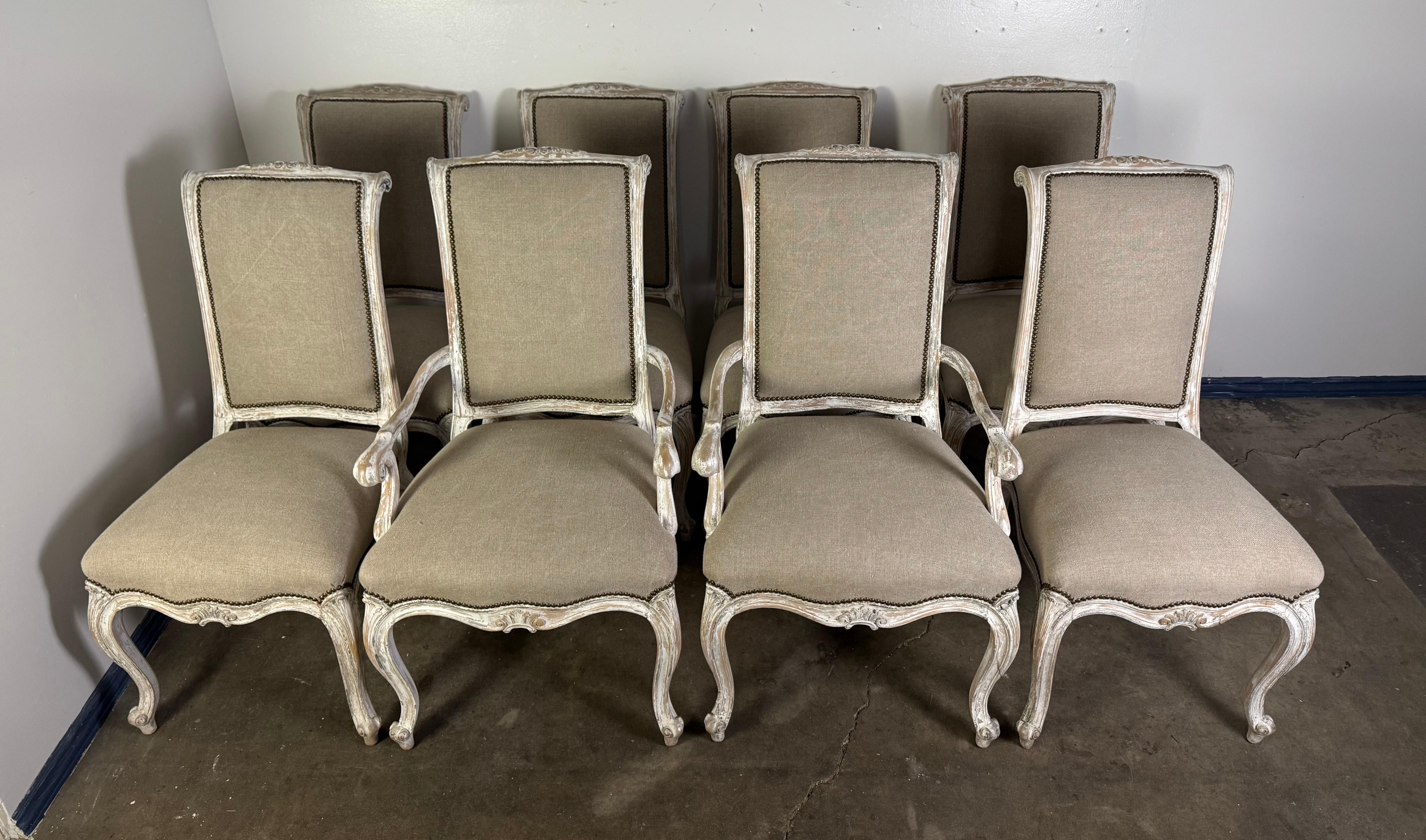 Cet élégant ensemble de huit chaises de salle à manger françaises présente un style Louis XV classique avec des pieds cabriole légèrement incurvés, des motifs floraux sculptés et une finition peinte en blanc vieilli qui révèle les nuances du bois
