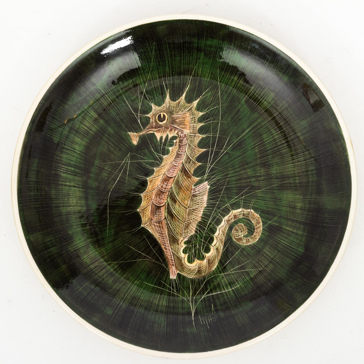 Set of French painted plates by artist Maoi depicting detailed sea life including seahorses, fish, and crabs, circa 1960. The set consists of one large platter and seven smaller plates. The size of the larger service plate is 24.00 inches wide by
