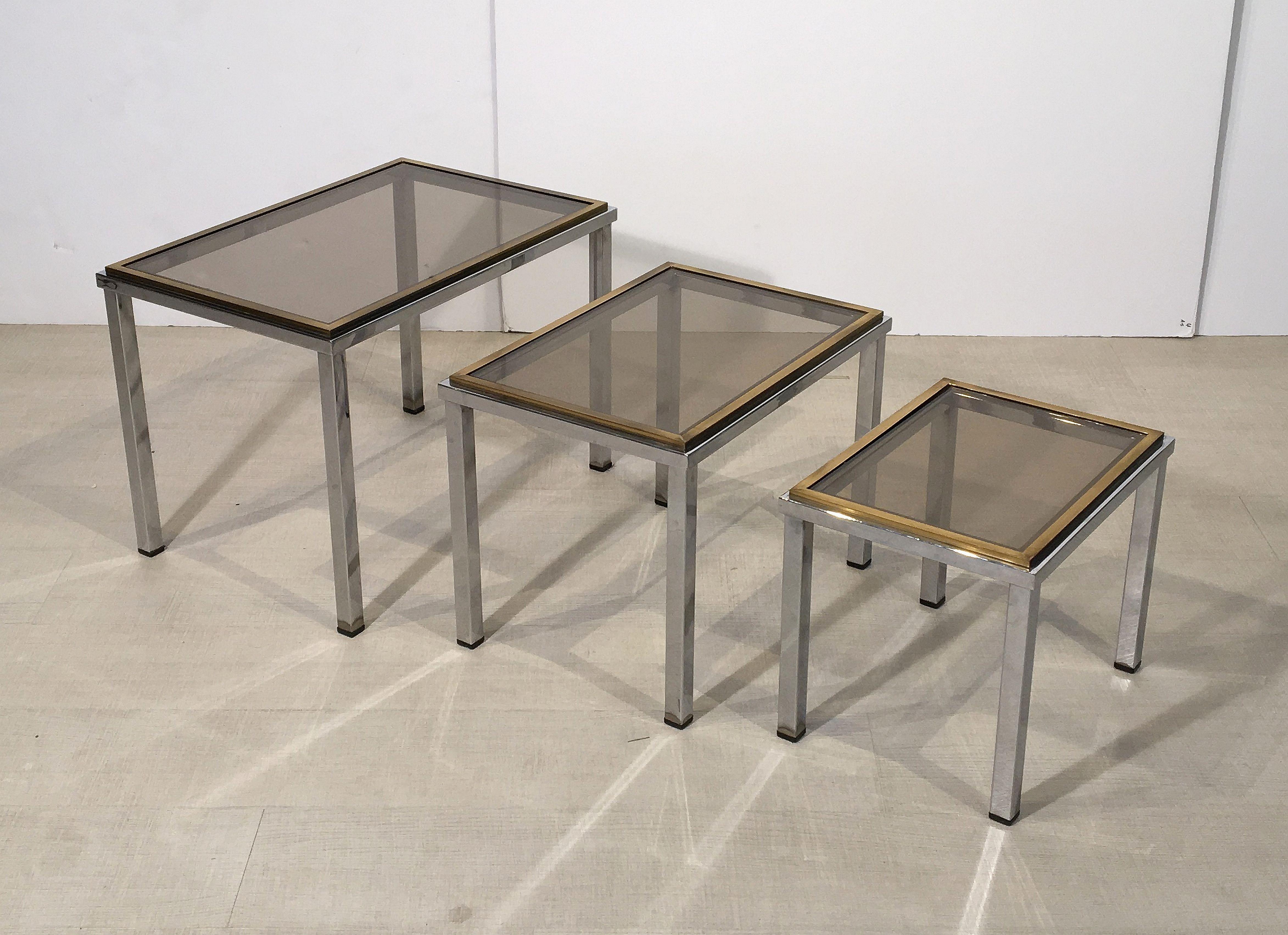 A fine set of French rectangular stacking or nesting low tables featuring three fitted tables, each with a design in brass and chrome with inset rectangular smoked glass top.

Great for use as cocktail or coffee tables as well.

Measures:
Large