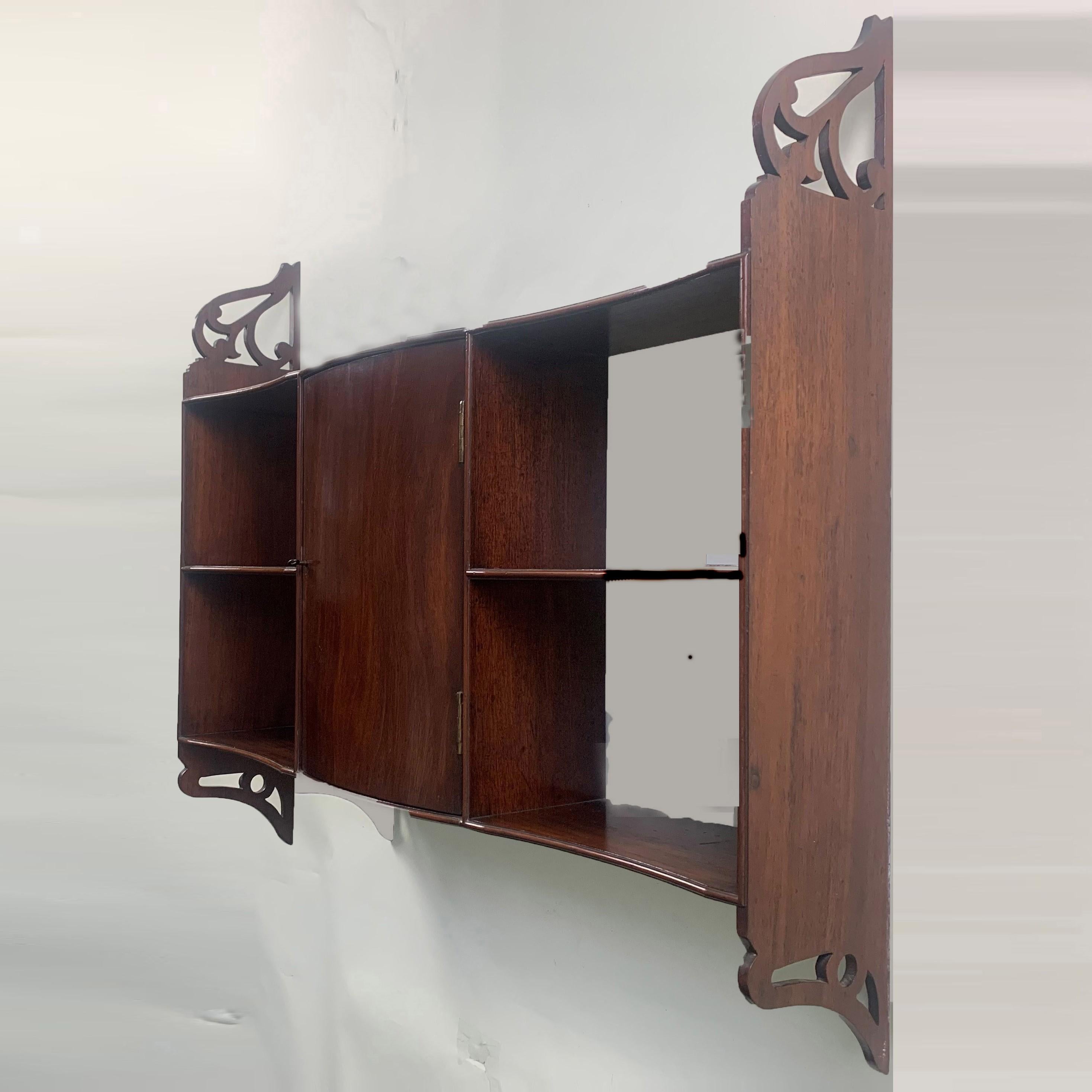 An unusual and attractive George III period set of serpentine fronted mahogany hanging wall shelves. With central, bow-fronted cupboard door and shelves either side, joined by fret-cut sides.