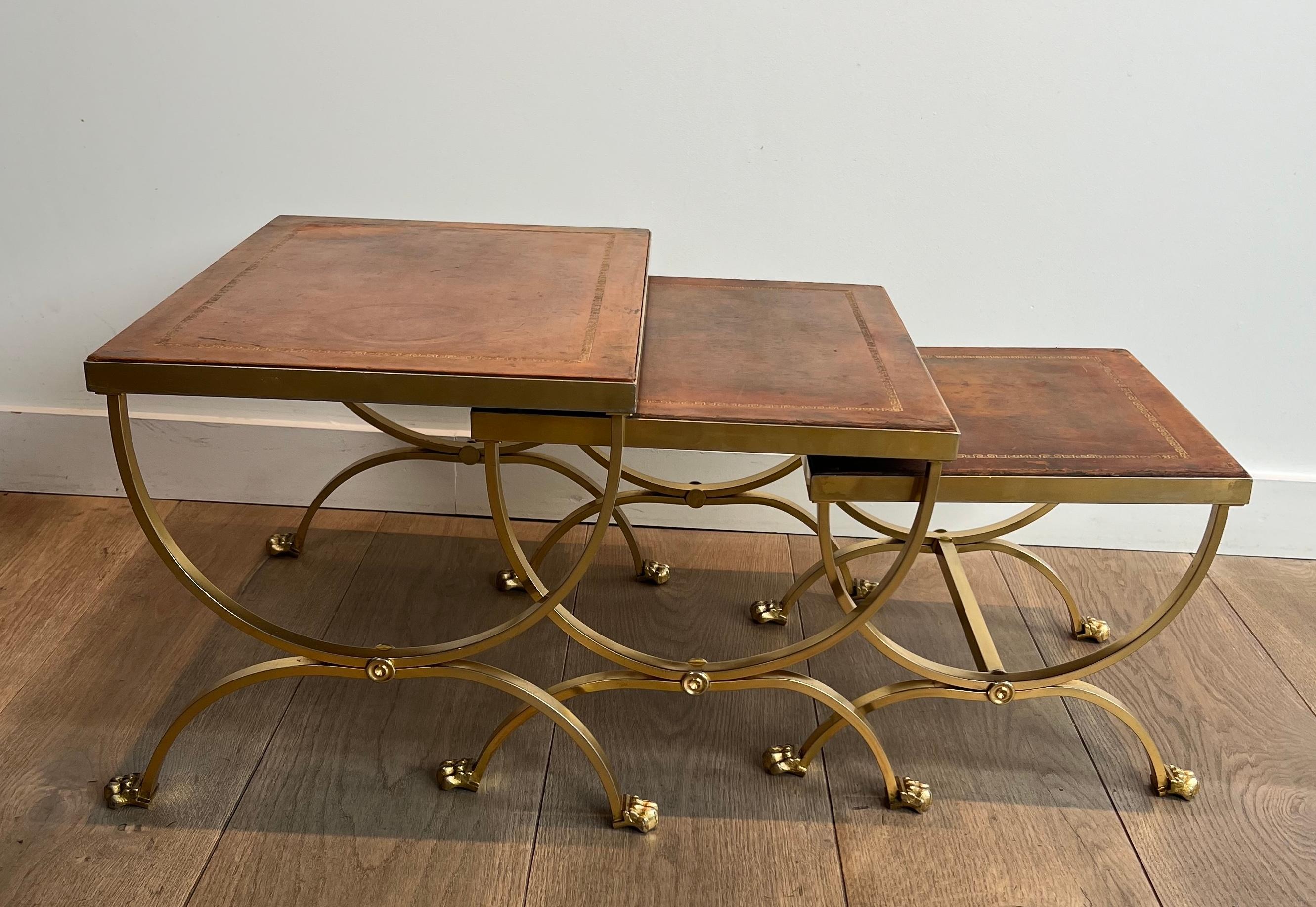 This rare and very nice set of nesting tables is made of gilt metal with claw feet and brown leather tops. This is a French work attributed by Maison Jansen. Circa 1940