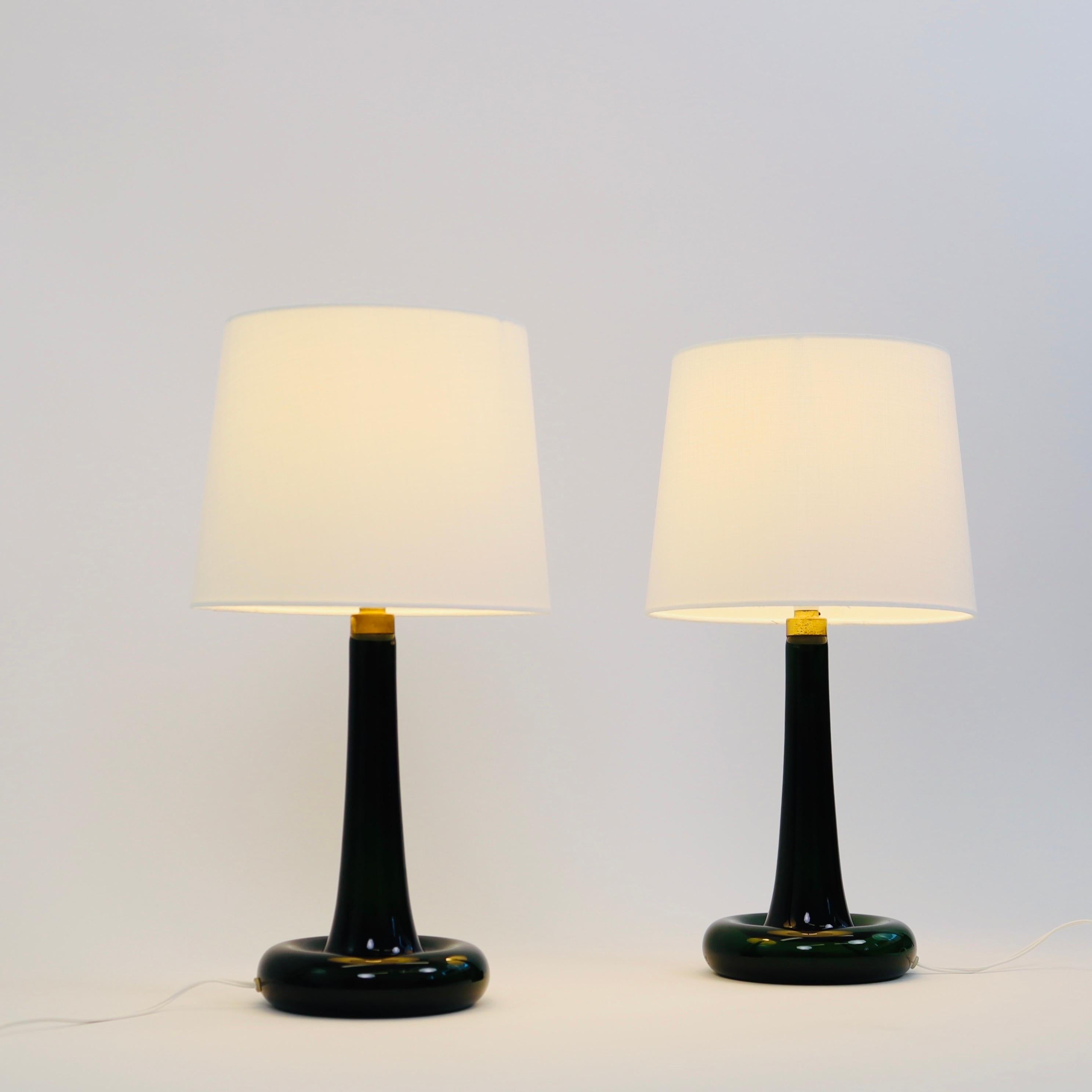 Set of classic dark green desk lamps designed by Michael Bang for Danish Holmegaard Glasværk in 1975. 

* A pair of green glass table lamps with brass details and white fabric shades
* Designer: Michael Bang 
* Style: Fleur
* Producer: Royal