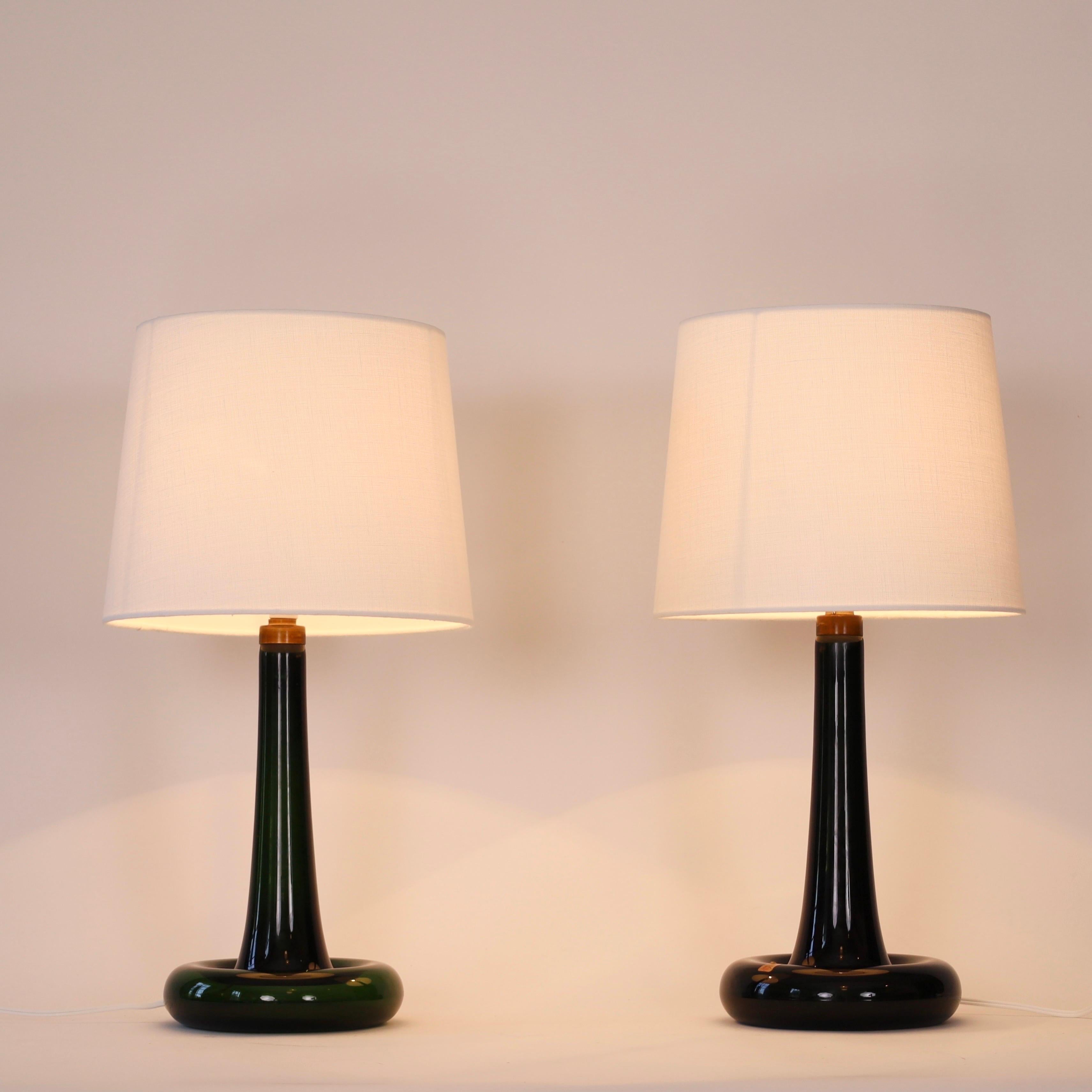 Ensemble de lampes de bureau vert foncé conçues par Michael Bang pour le danois Holmegaard Glasværk en 1975. Un bel ensemble pour un bel espace.

* Paire (2) de lampes de table en verre vert foncé avec détails en laiton et abat-jour en tissu blanc
*