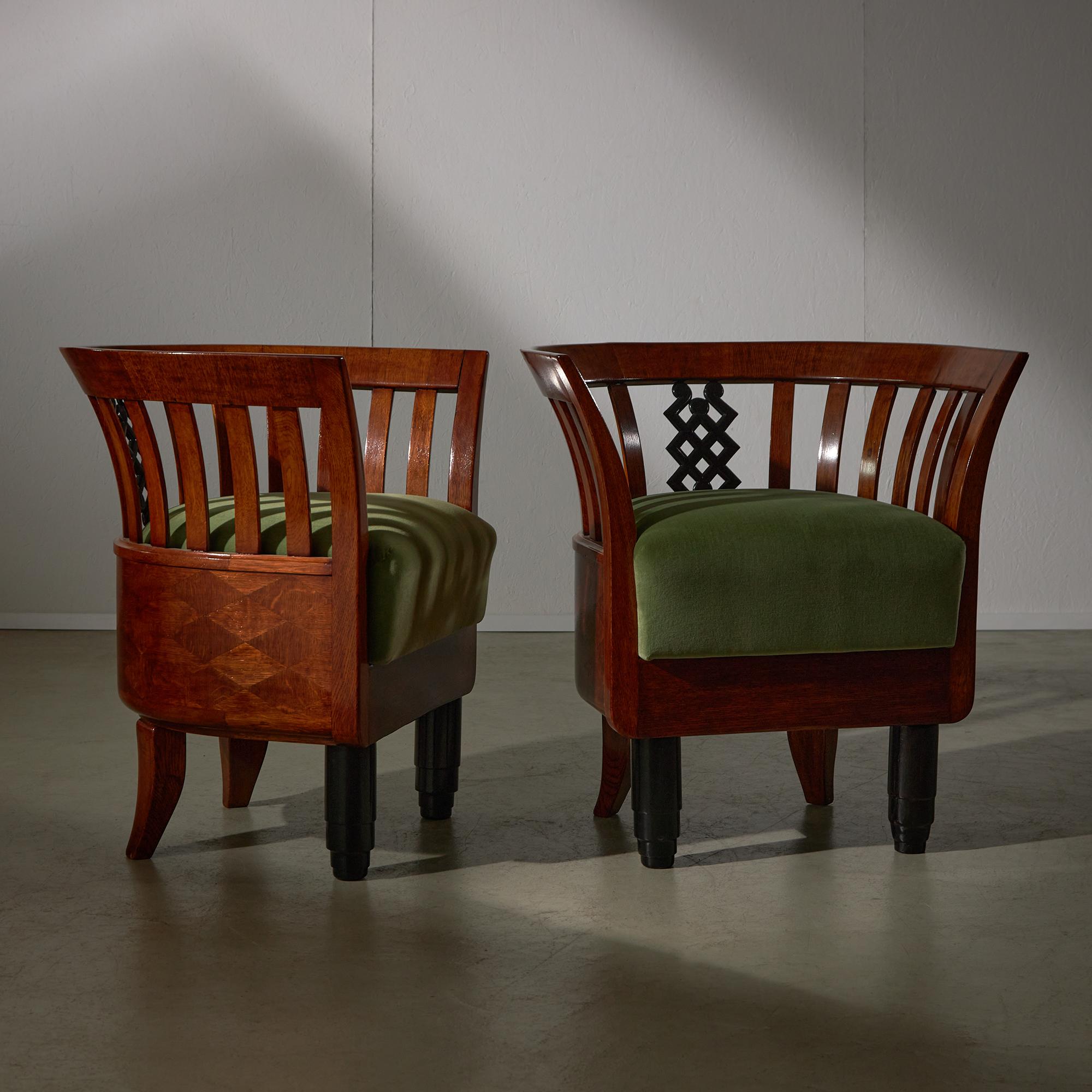 This impressive  Art Deco Armchair duo dressed in green velvet upholstery is complemented by intricate wooden decorative accents. Made of quarter-sawn oak, favored in furniture making due to its stability and attractive look. The warm, reddish-brown