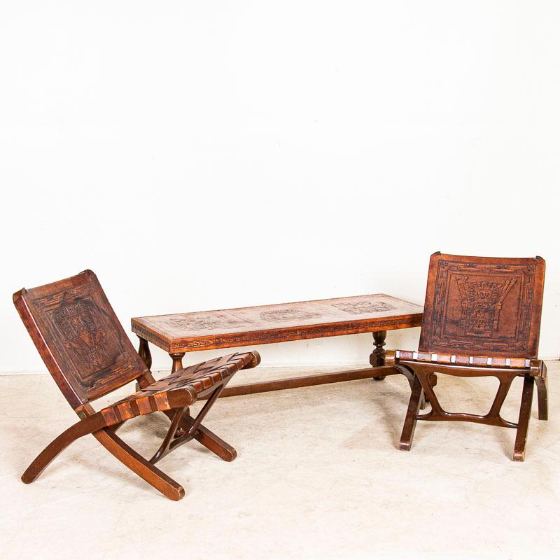 This fabulous vintage set of 2 folding chairs and coffee table are made of hand-tooled leather. Note the detailed figures reflective of Aztec or South American gods or warriors and the deep patina of the worn leather. The seats of the chairs are