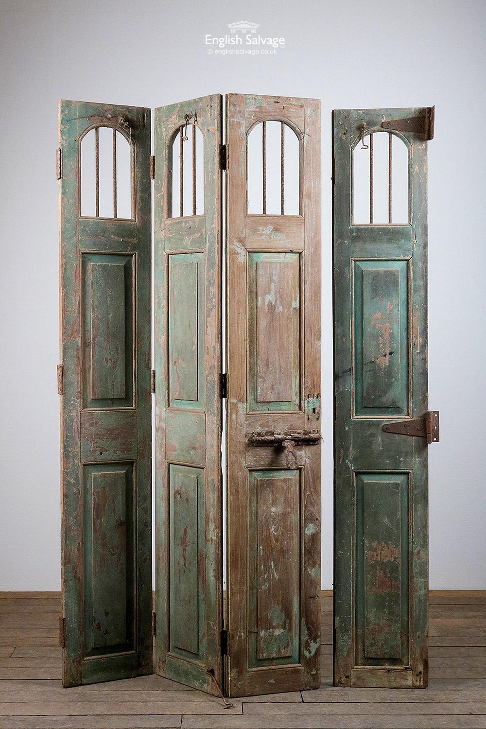 Set of reclaimed Indian hardwood paneled folding doors / shutters. Comprises of a triple folding section and one end piece (slighter shorter at 180cm high). Arched window detail to the tops with iron bars (no glass). Traces of green paint. Triple