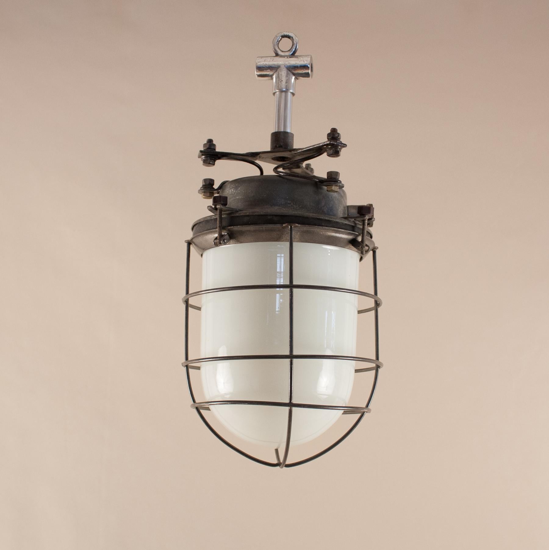 A group of six 1960s maritime ship's galley pendant lights from Eastern Europe, each with a milk glass capsule housed in a steel cage and topped with a shock-absorbing steel assembly cap. The replaced aluminum stem is optional. These midcentury