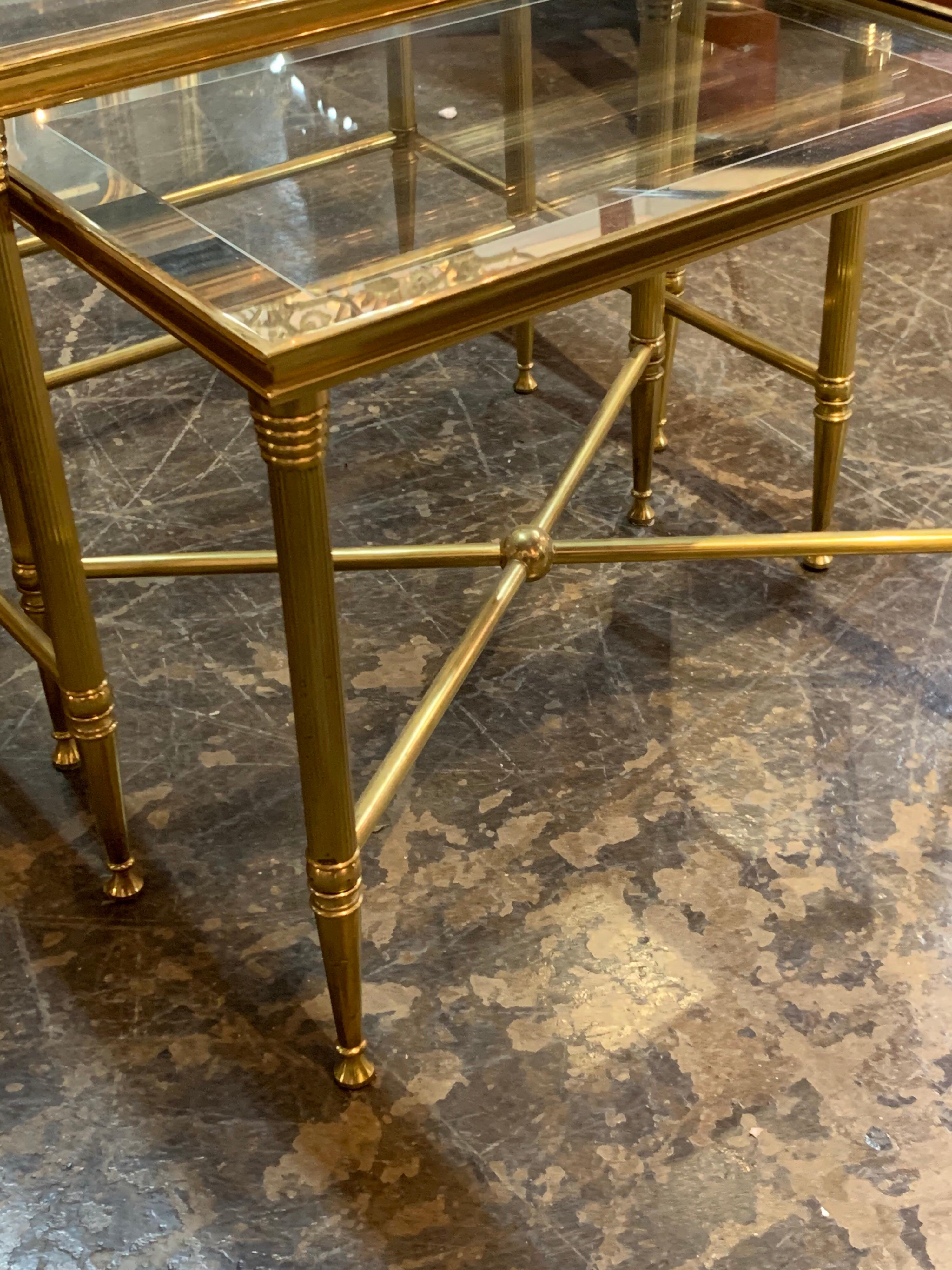 Lovely set of brass and glass top nesting tables. There is mirrored glass on the outside edges of the glass top and nice details on the brass bases. A very pretty Classic look!
        