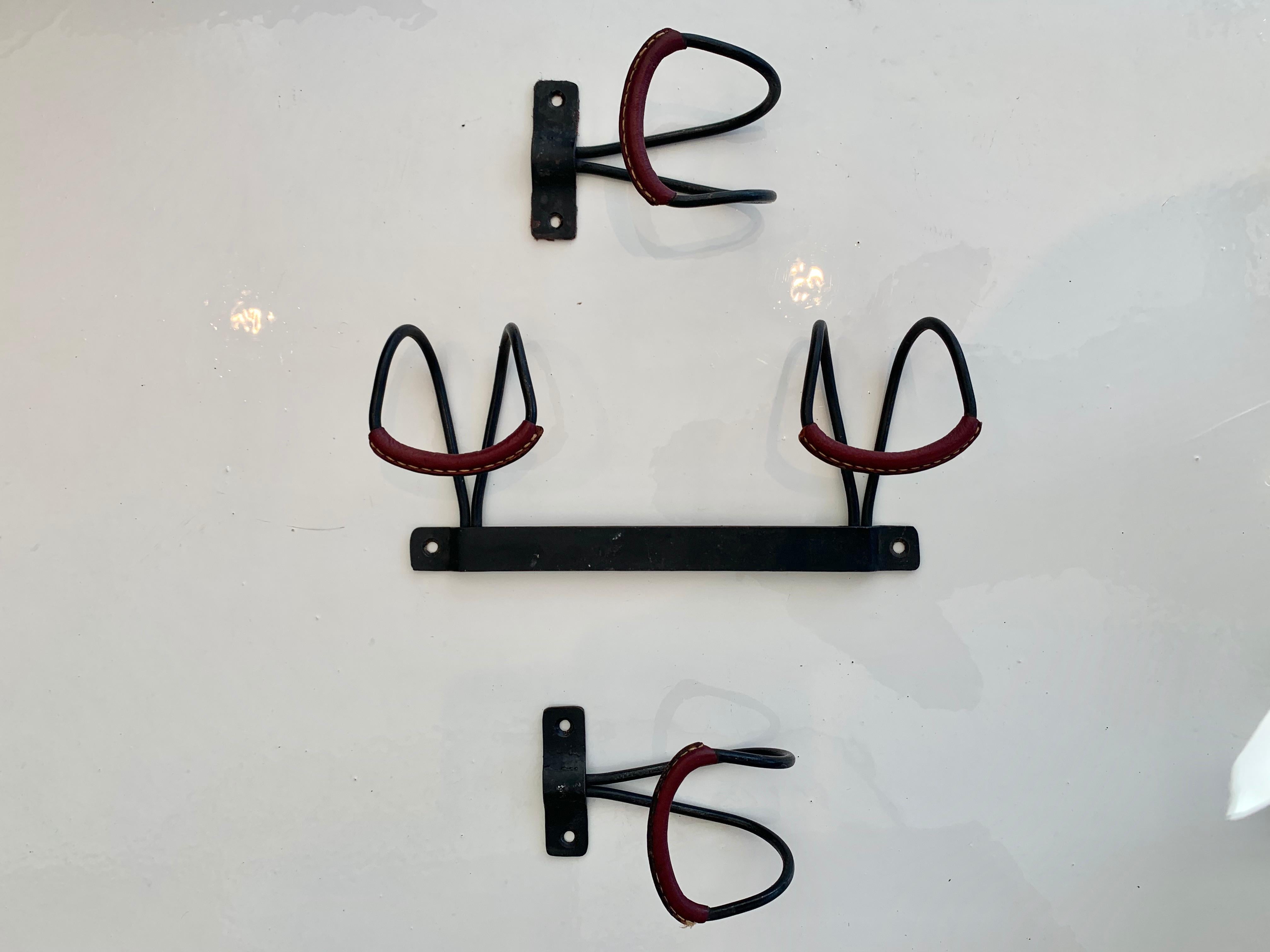 Excellent set of hooks by French designer Jacques Adnet. Iron frame with red leather wrapped hooks. One double hook. Two single hooks. Signature Adnet contrast stitching. Great vintage condition. 

Sold as a set of three hooks.