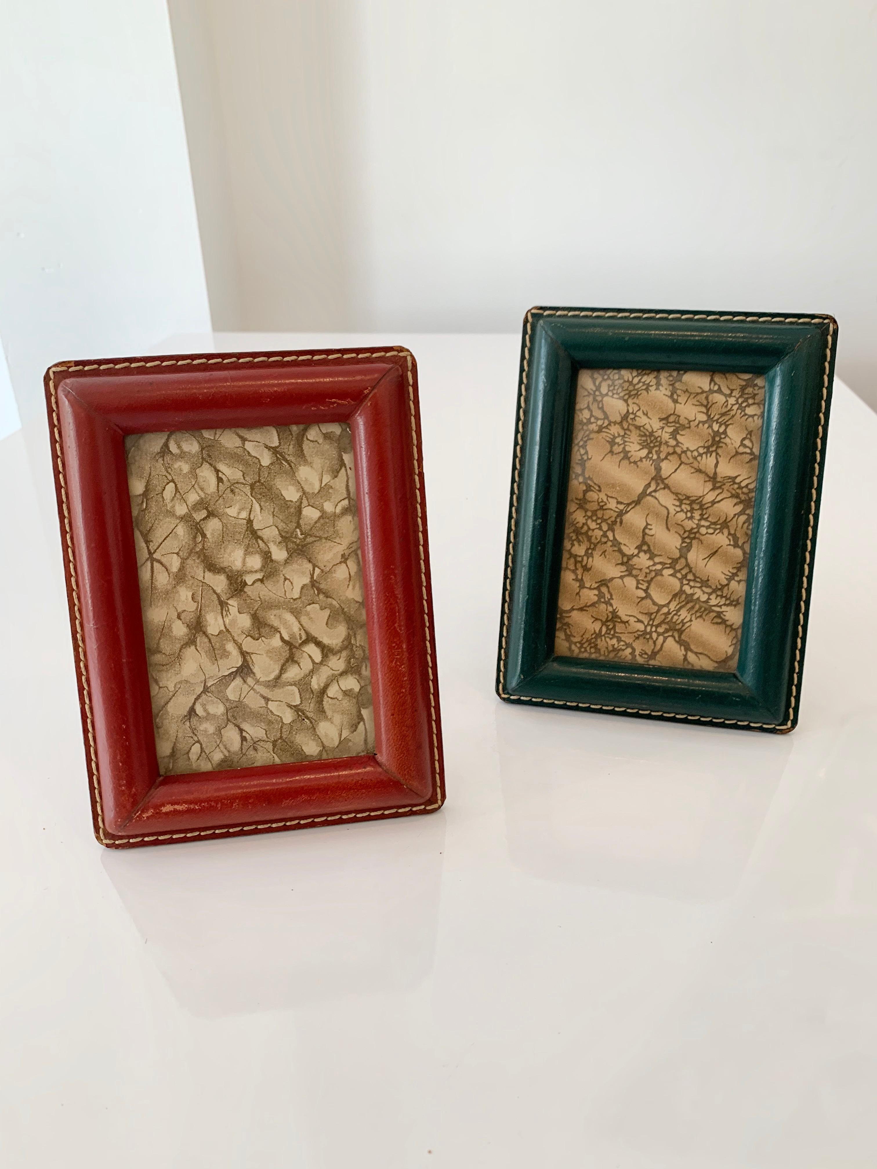 Handsome French leather picture frames by Jacques Adnet. One in green and the other in red. Signature Adnet contrast stitching. Very good vintage condition. Great patina and age to leather. Priced as a pair.