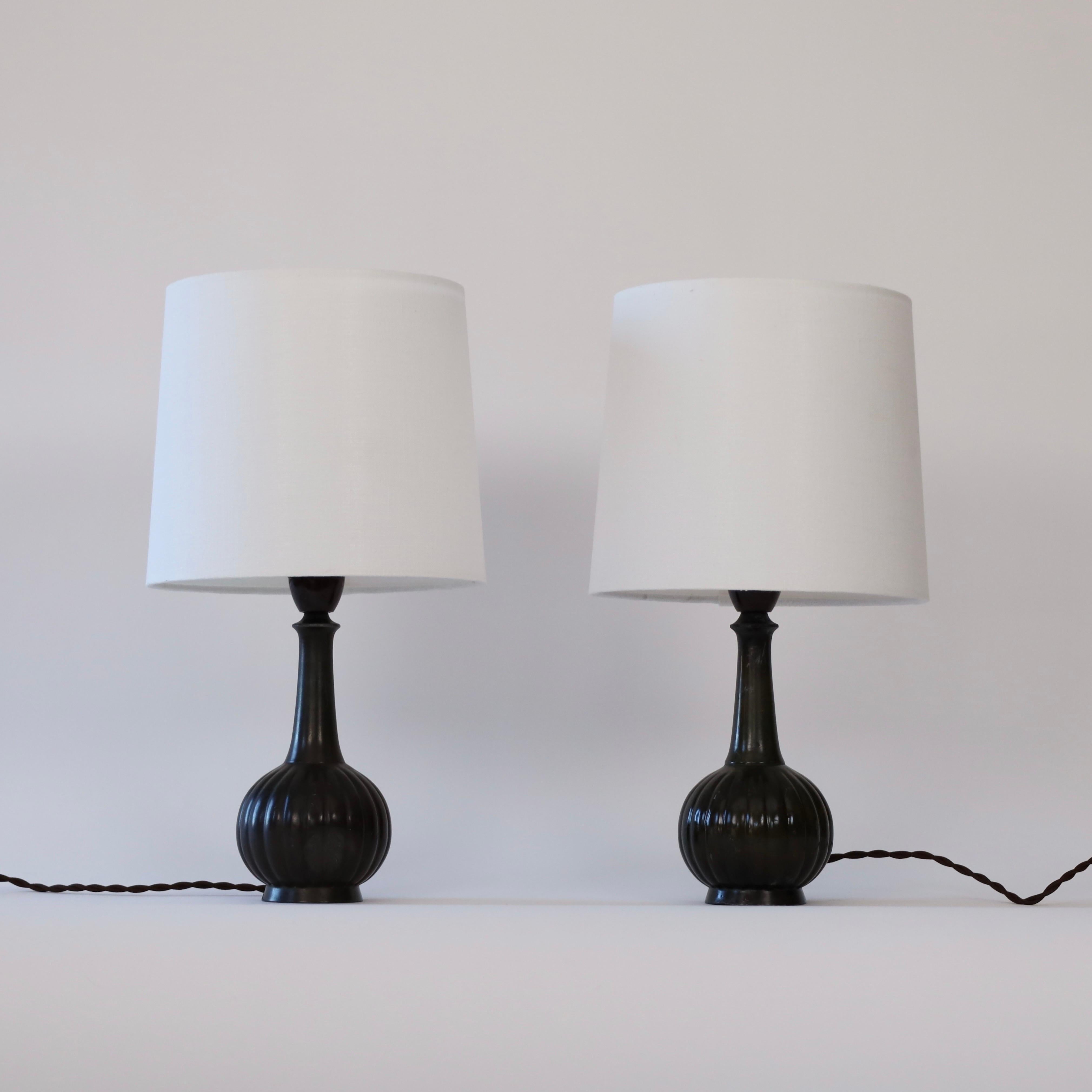 Set of 1920s Just Andersen desk lamps. A historic duo with marks from a 100 years life-time.
 
* A set (2) of metal desk lamp with a round base with vertical lines and white shades.
* Designer: Just Andersen
* Model: D140 (stamped ‘Just D140’)
*