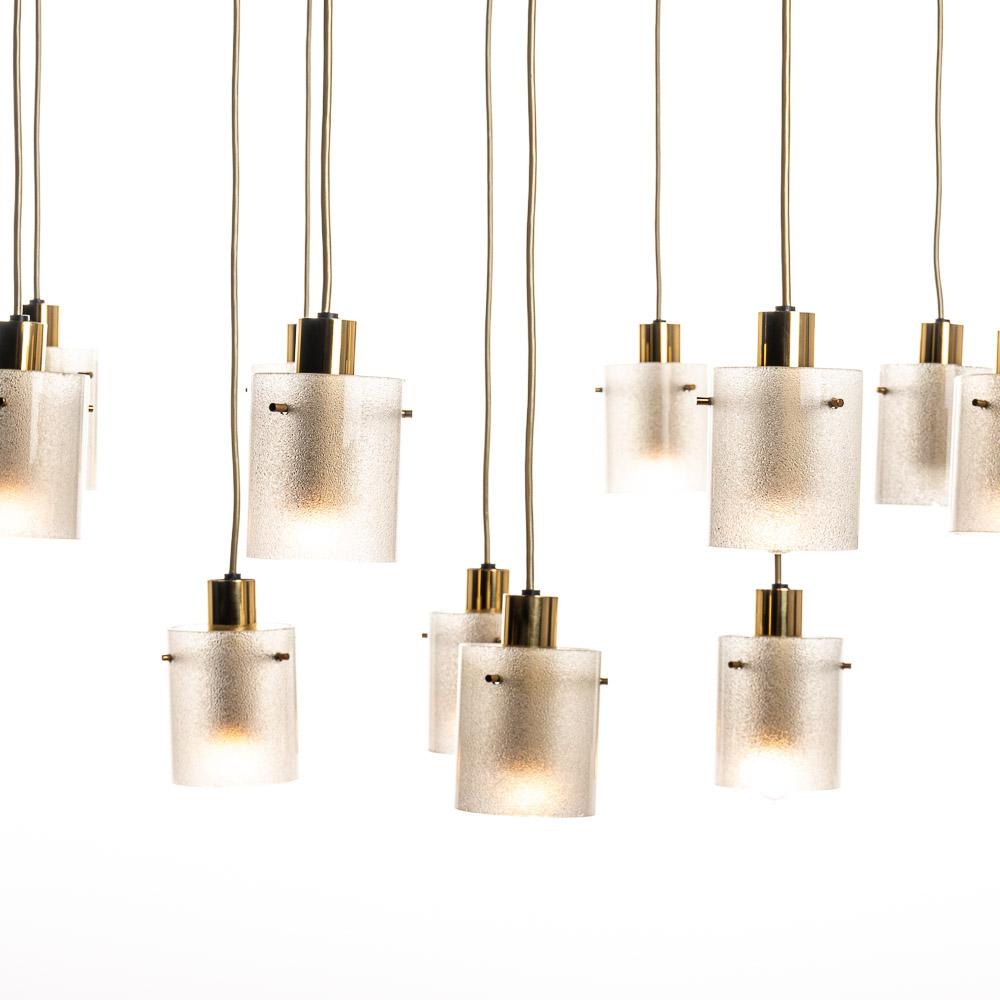 Stylish chandelier consists of 12 'arms' with beautiful pressed glass cylinders. The cylinders are roughly  textured on the inside. The combination of the brass, glass  and the long length of the wiring, make it an eye catcher! 