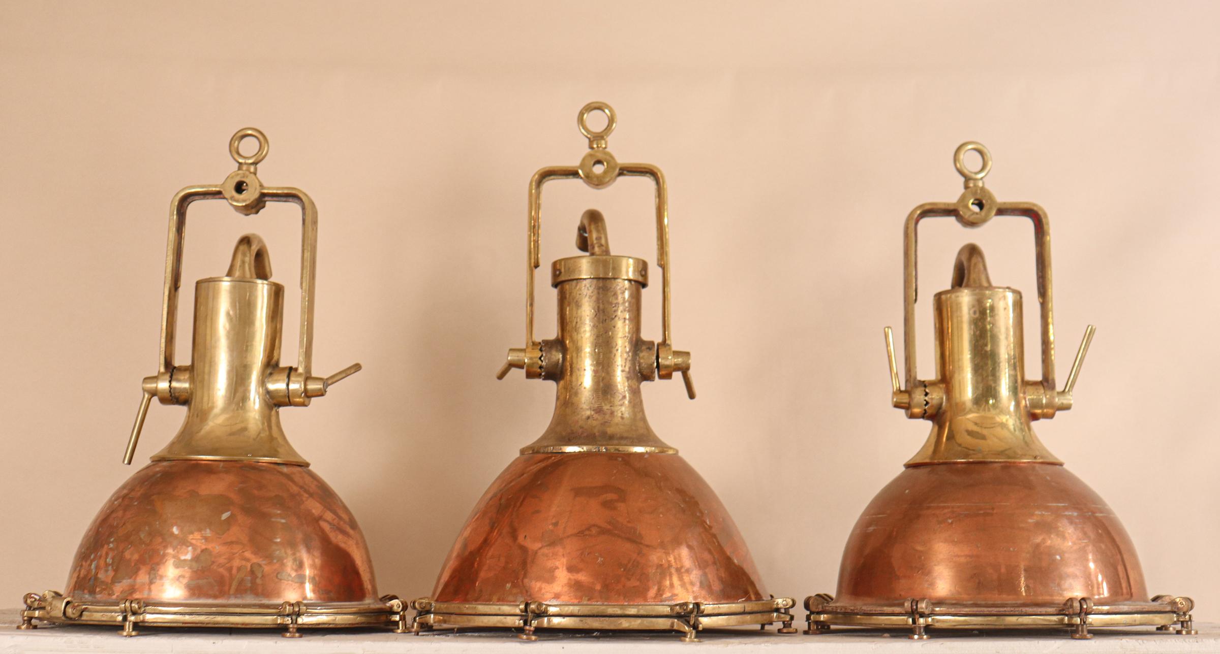 An authentic set of large copper and brass ship's deck lights with superb form and patina, circa 1950. Salvaged from a maritime vessel and attentively restored to near-original condition, these nautical pendants suspend from adjustable solid brass