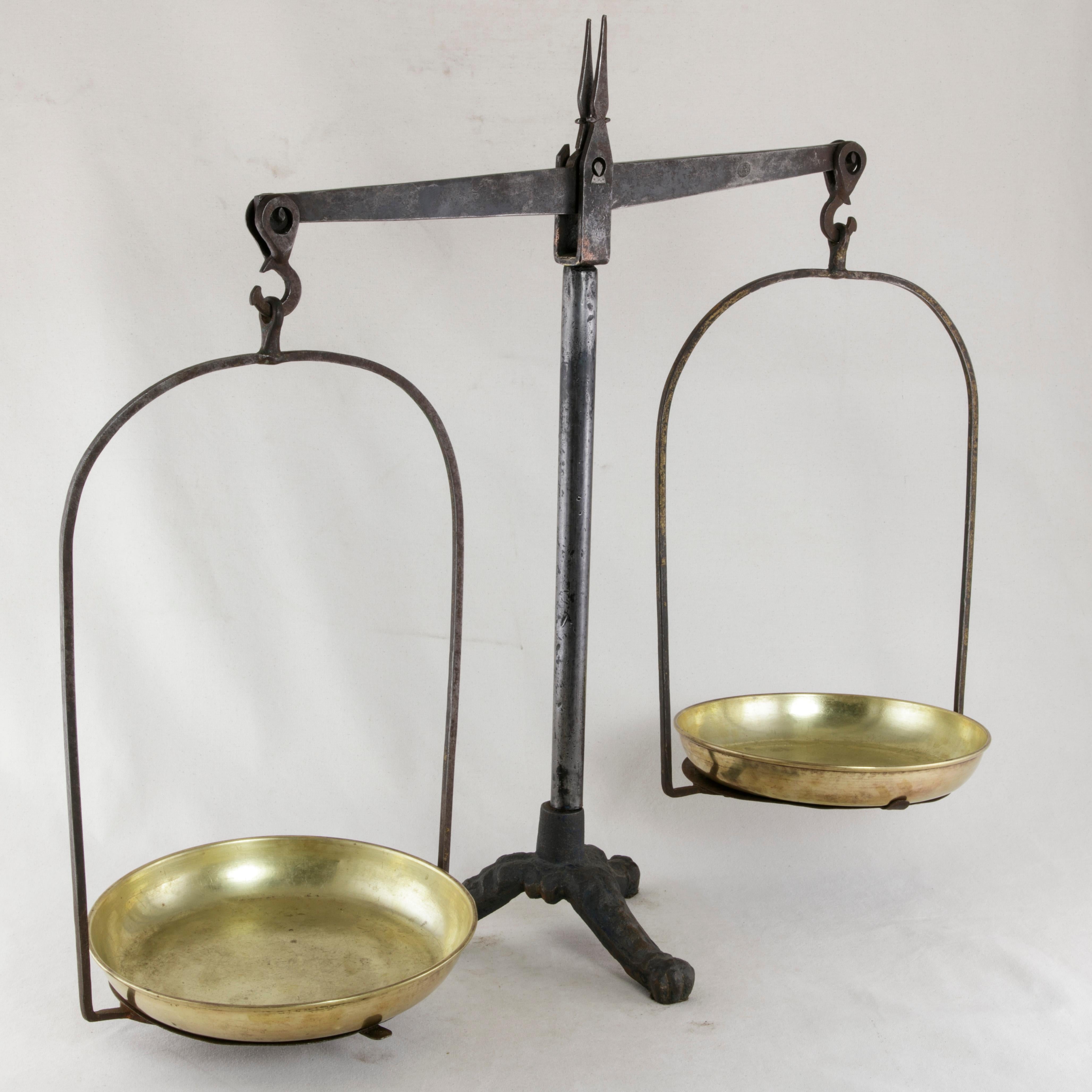 From the region of Normandy, France, this set of late 19th century iron scales features its two original brass pans. The central iron rod rests on a cast iron tripod base detailed with leaves and finished with claw feet. A wonderful decorative