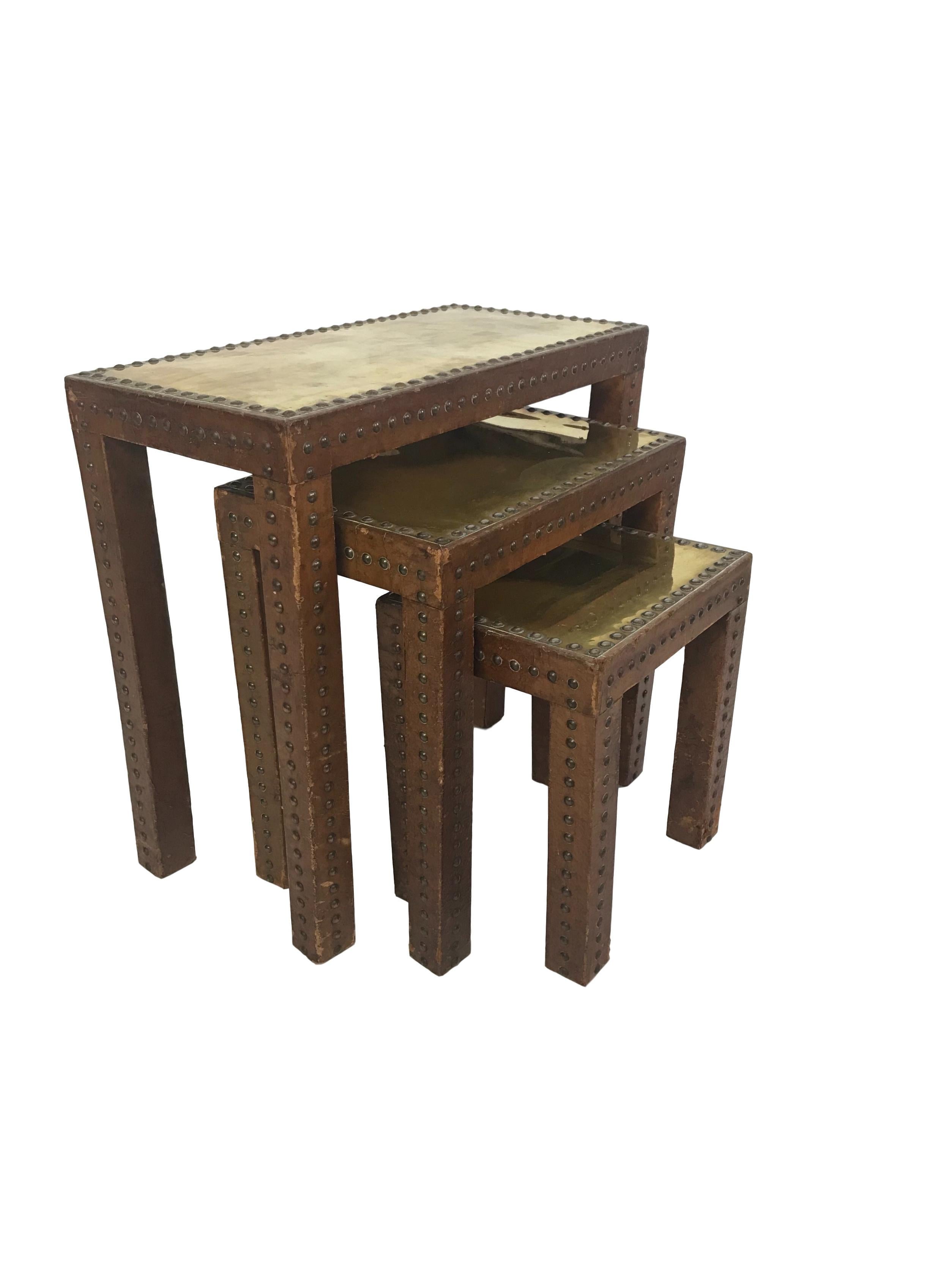 This is a fantastic one of a kind set of leather and brass studded nesting tables. The tables are wrapped in a worn rich colored cognac leather with brass studs that adorn the legs and tops. The table tops are made of brass plates held in place by