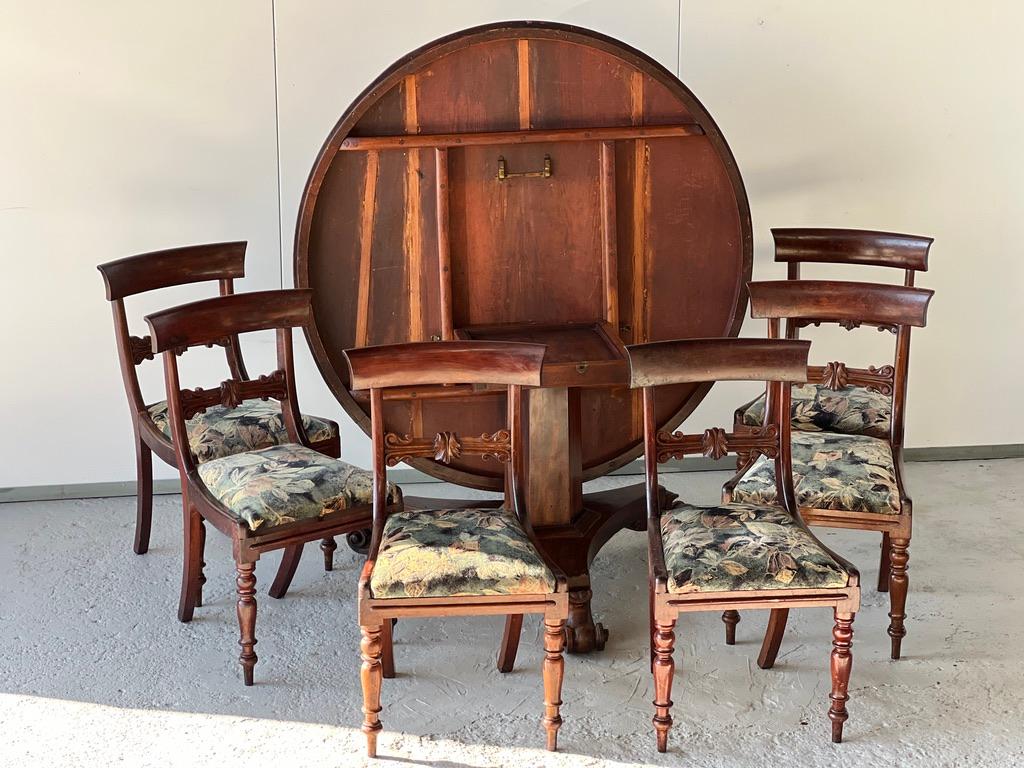 Mahogany dining set, English work, 19th century, including a round table with tilting top and 6 carved mahogany chairs with removable fabric seats. 

English mahogany table on castors early 19th century
Dia 135 cm 
Height 70 cm 
English chairs