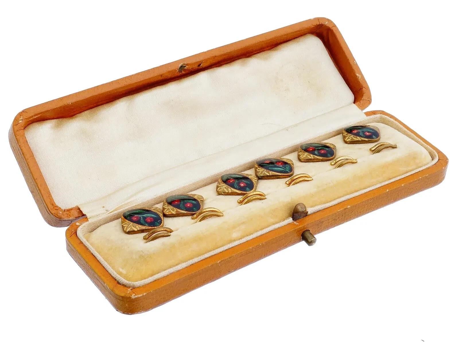 Un set di tre paia di gemelli vintage della metà del secolo, ornati da smalti a motivi floreali dipinti a mano su metallo dorato. Non segnato. Presentato nella sua scatola originale. Gioielli, regali e accessori vintage per uomini e