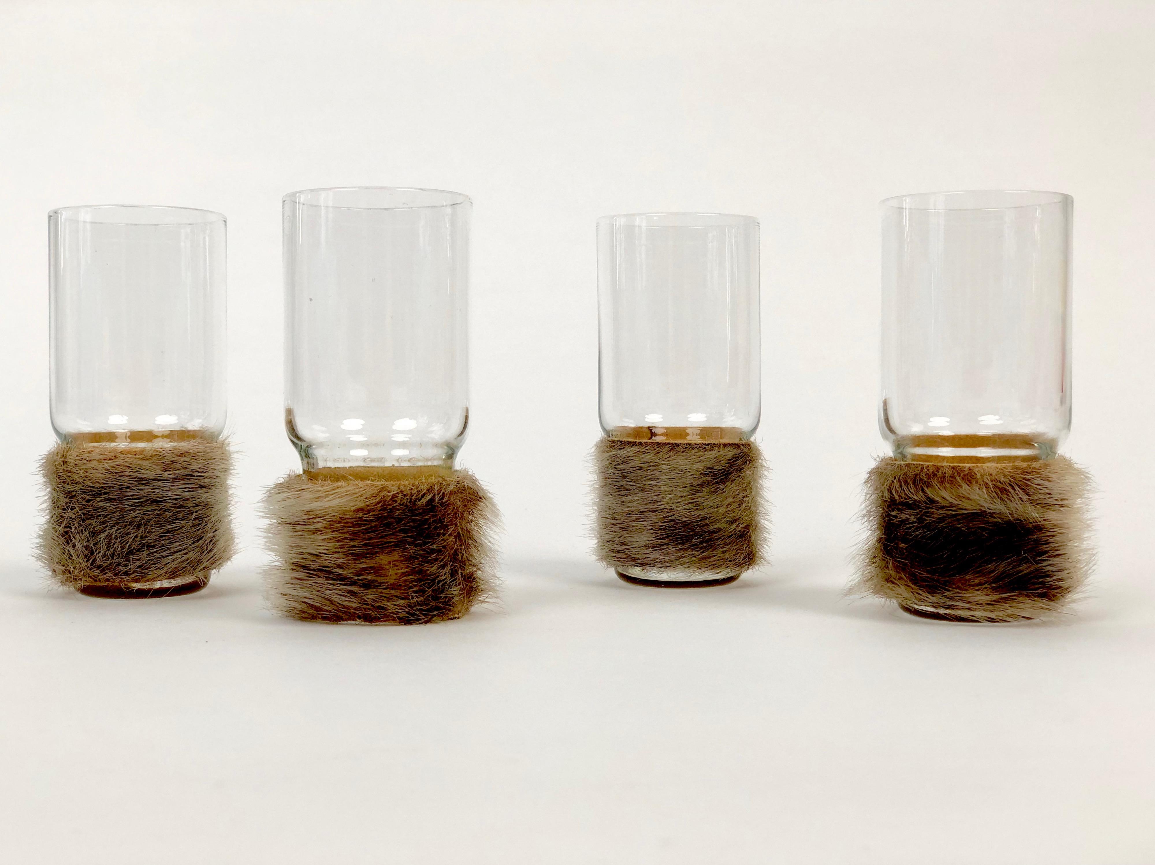 A set of four Drinking glasses with their bases wrapped in fur. These glasses were hand blown by the company Edelweiss.
The design is perhaps from or inspired by Carl Auböck. The fur sleves can be removed for cleaning.
The glasses are in very good