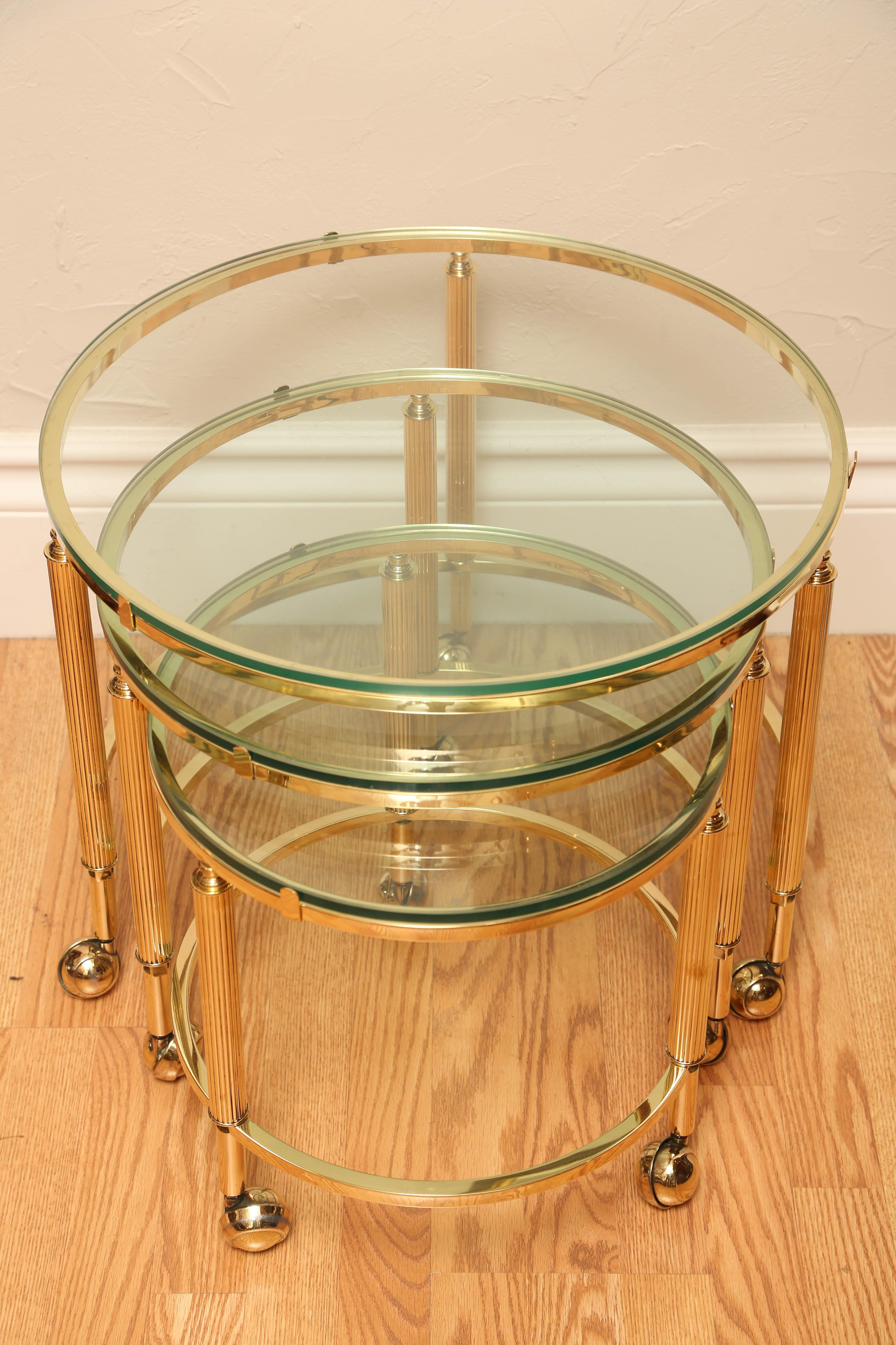 Mid-Century Modern round brass stacking tables with fluted legs, original brass castors and glass tops.