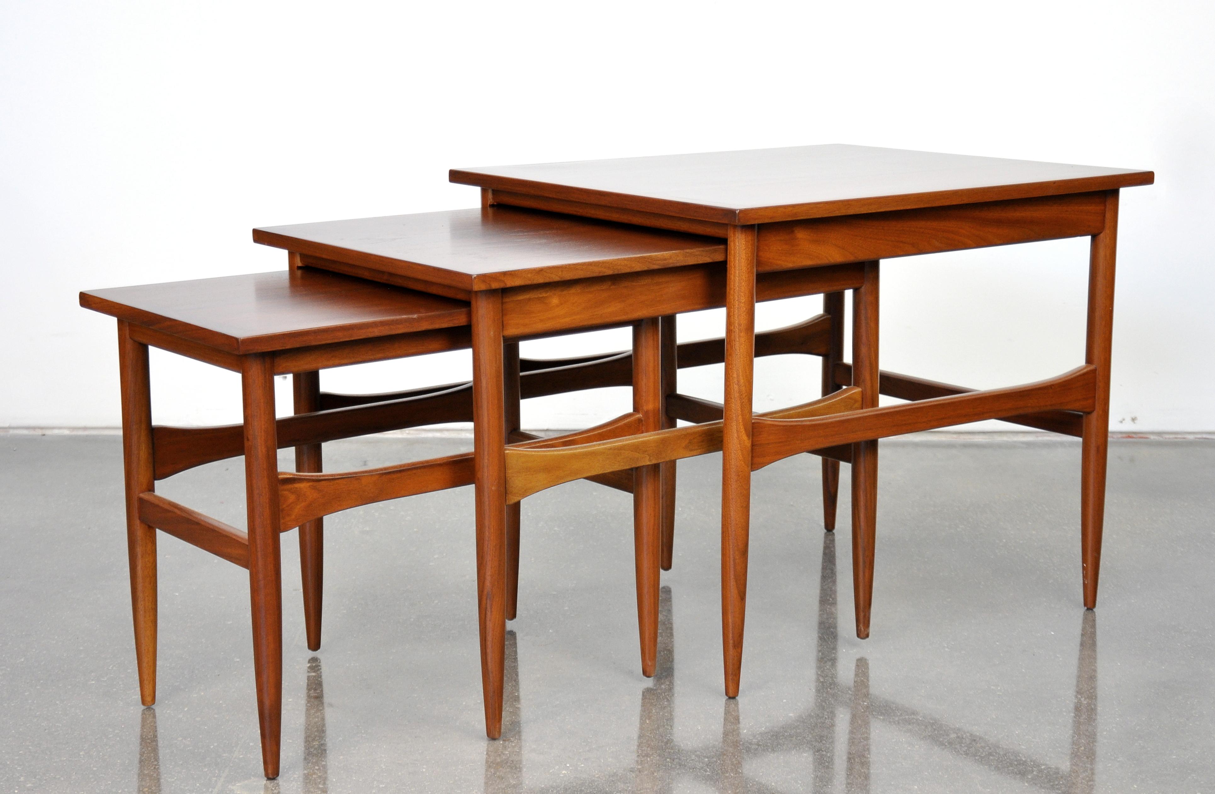 A vintage Danish modern set of three side tables dating from the 1960s. Each end table has a shaped spanner connecting the tapered legs. Medium occasional table measures 18.25 in x 14.5 in x 19 in H, smallest table measure 14.38 in x 14.13 in. x