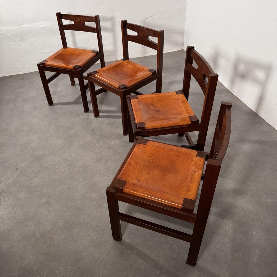Set of solid wengé dining chairs. Beautiful drawings in its wood. Nice thick patinated saddle cognac colored leather seats.

The leather has wear but no holes, tears or damages. Just the blots and stains that you can expect on mid century cognac