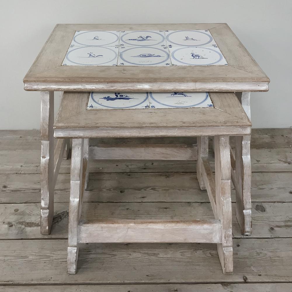 Set of midcentury tile-top nesting whitewashed tables gives you two tables for the price of one! Handcrafted from solid oak to last for generations, the tops have been inset with hand painted 18th century delft tile for carefree rustic
