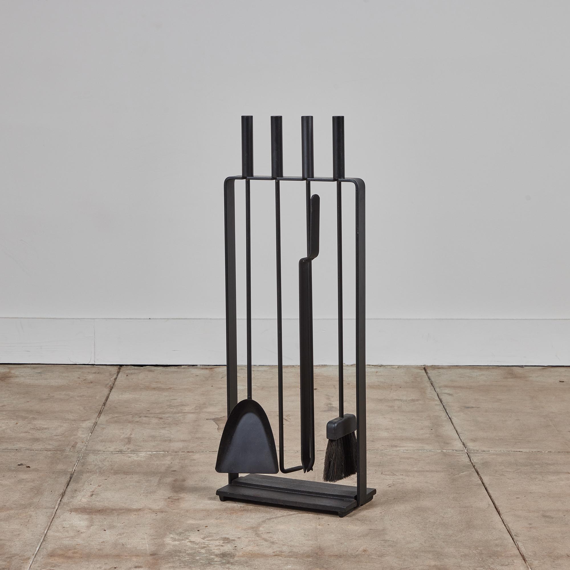 A five piece set of Pilgrim fireplace tools with stand, USA, c.1950s. The set features four tools with cylindrical handles and comes with a matching stand. All elements are made of blackened iron. This modernist piece shows off clean and minimal