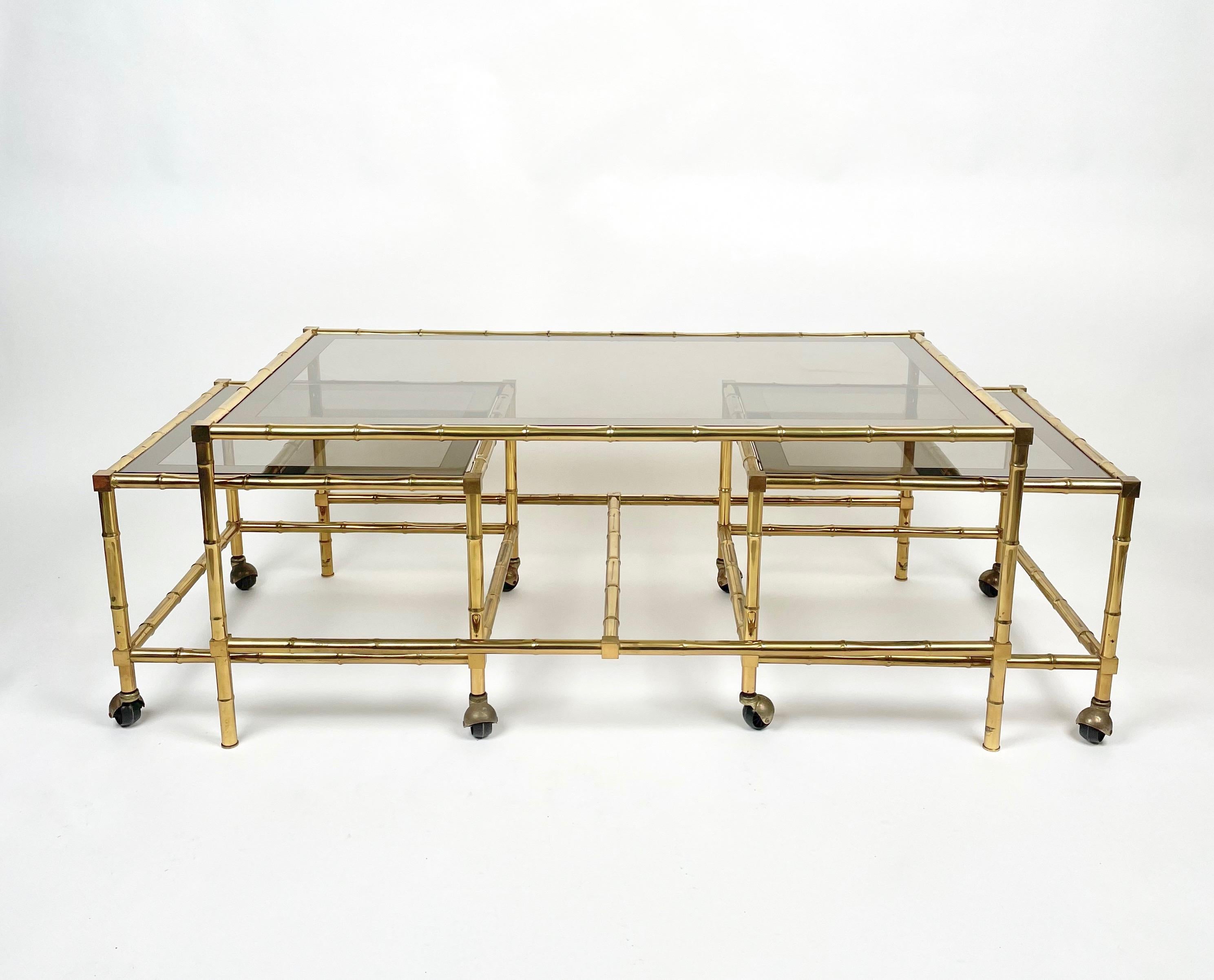 Rectangular coffee table nested with two squared coffee tables on wheels - which can be moved - featuring a brass, faux bamboo structure and smoked glass surface framed by mirror. In the style of the French house Maison Bagues, made in Italy in the