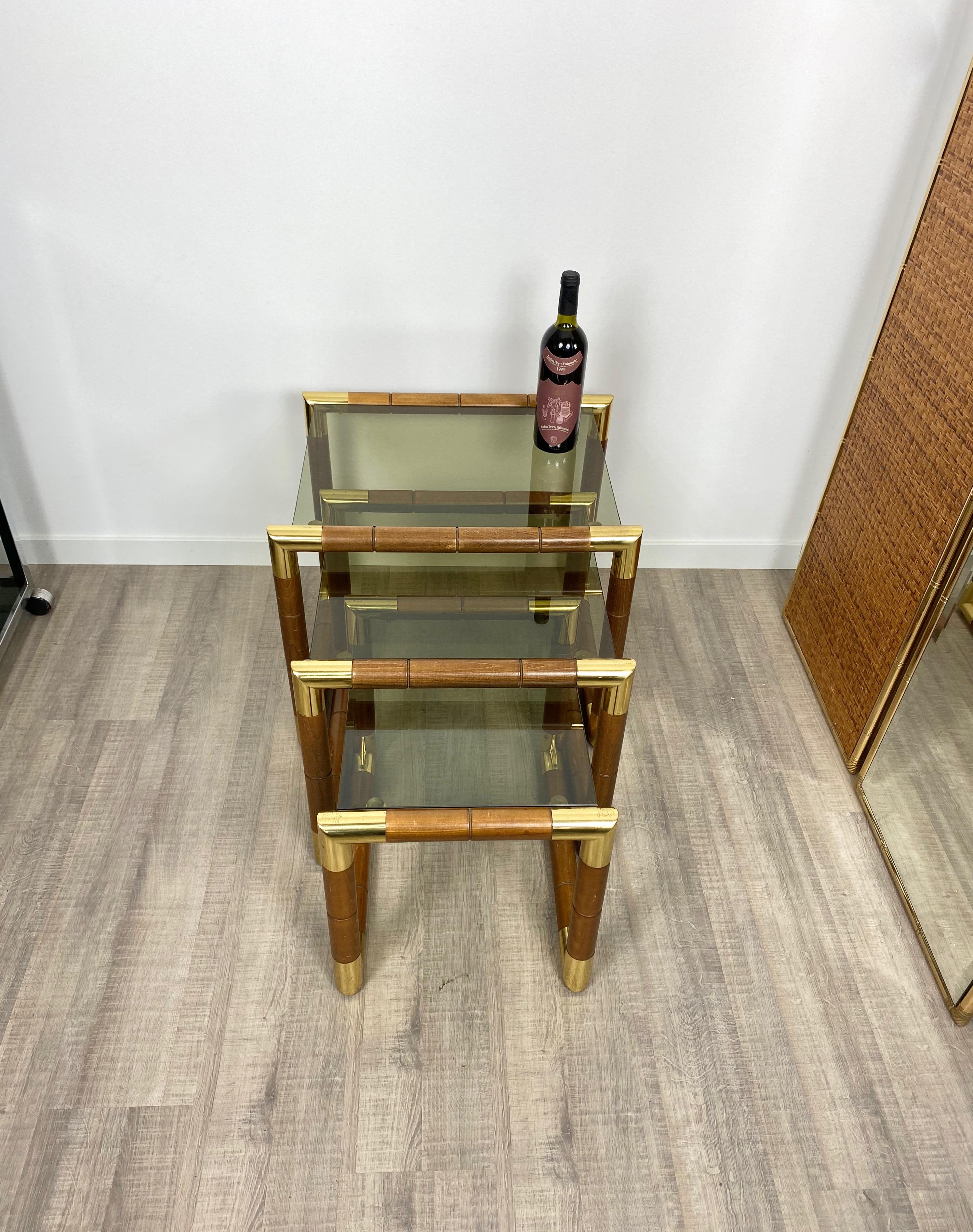 Three nesting tables featuring a wooden structure with brass corners and glass shelves in decreasing sizes. 

Dimensions: 
Biggest: 47cm height x 56 width x 47cm depth 
Middle: 43 x 46 x 47 cm
Smaller: 37.5 x 36 x 47 cm.