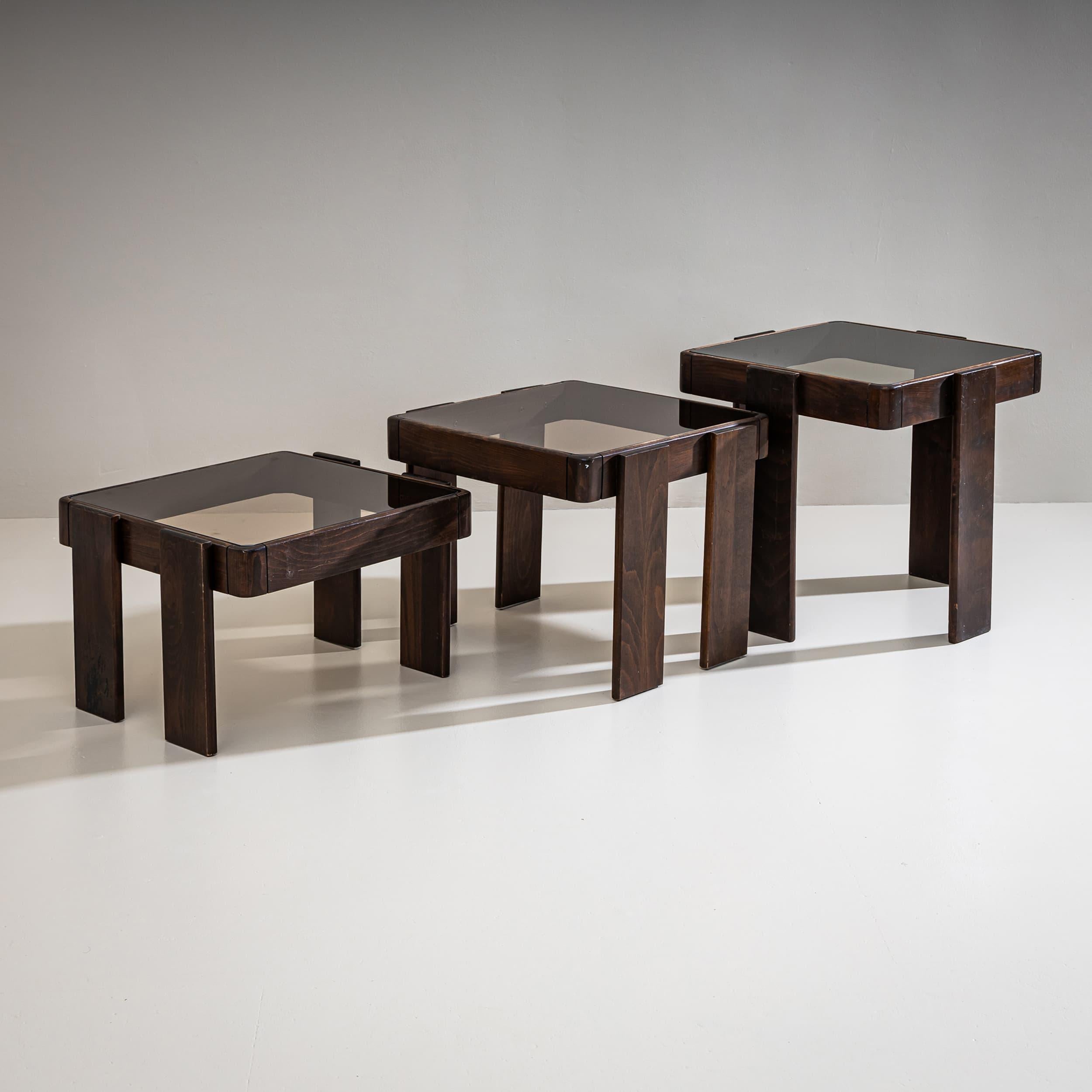 Set of three rectangular wooden nesting tables, each featuring a dark glass tabletop. The elegant design and functional form are characteristic of Gianfranco Frattini's style. Space-saving, stackable construction.