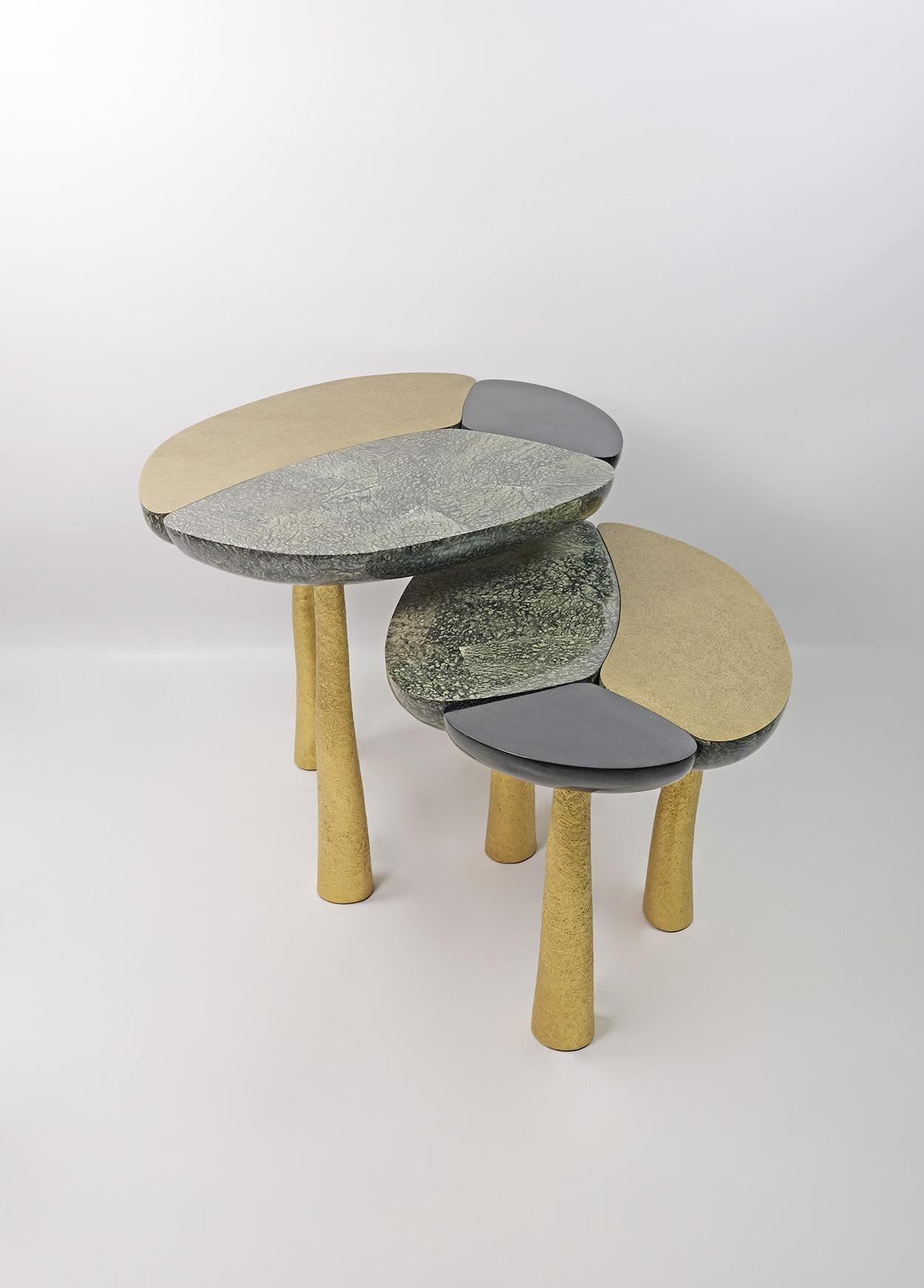 Dieses organische, moderne Set aus 2 Tischen besteht aus Baguio-Stein und schwarzen Muschelintarsien mit gehämmertem Messing auf der Tischplatte.
Die Beine sind aus Holz mit einer vergoldeten, halbrohen Glasfasereinlage.
Ein sehr einzigartiges