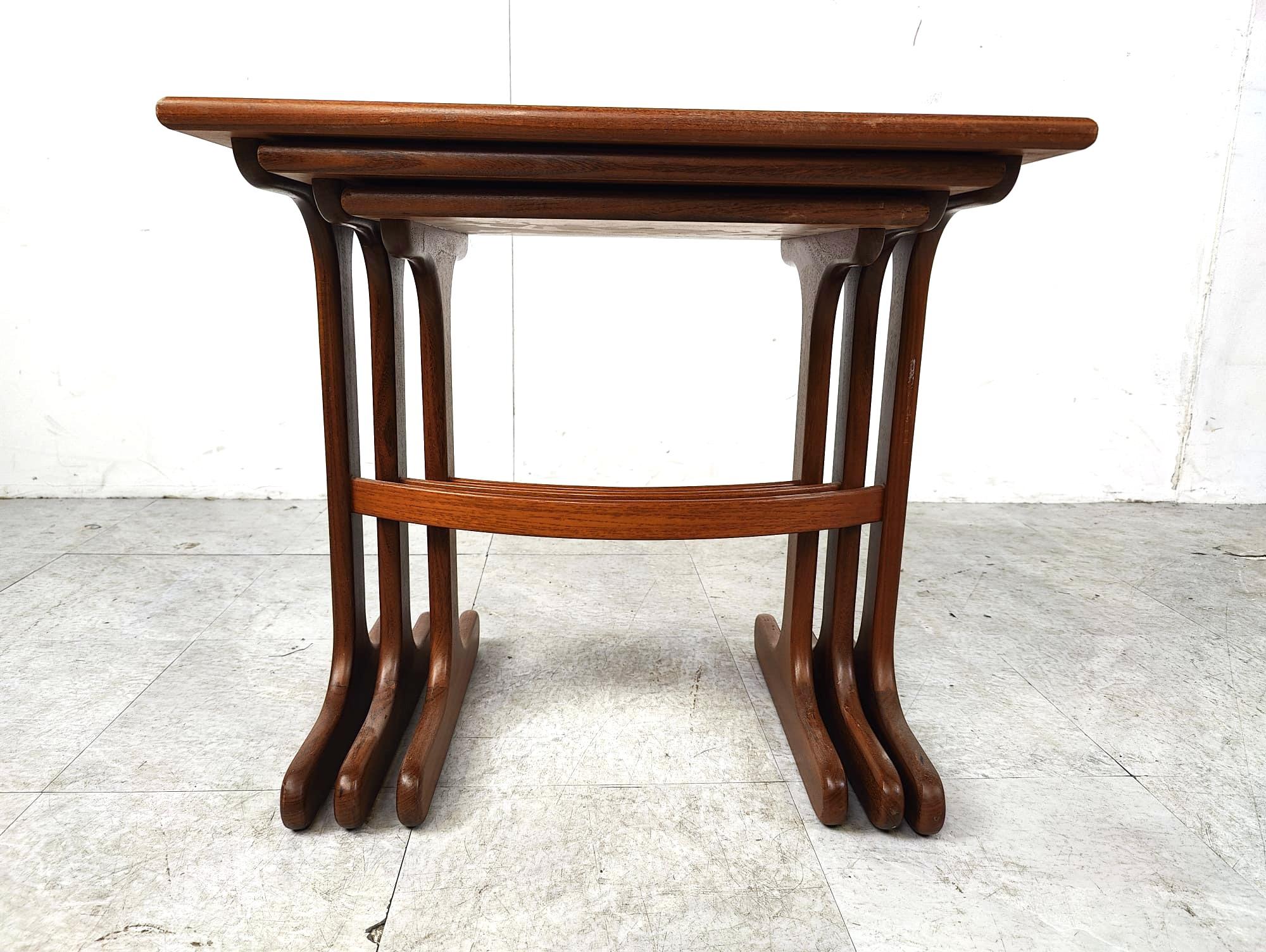 G Plan nest of 3 tables from the E Gomme furniture manufacturer. Each top is teak veneered and finished with solid teak edging, and each solid teak base has 2 stylishly fashioned pedestals which are connected by a curved stretcher. 

Beautiful