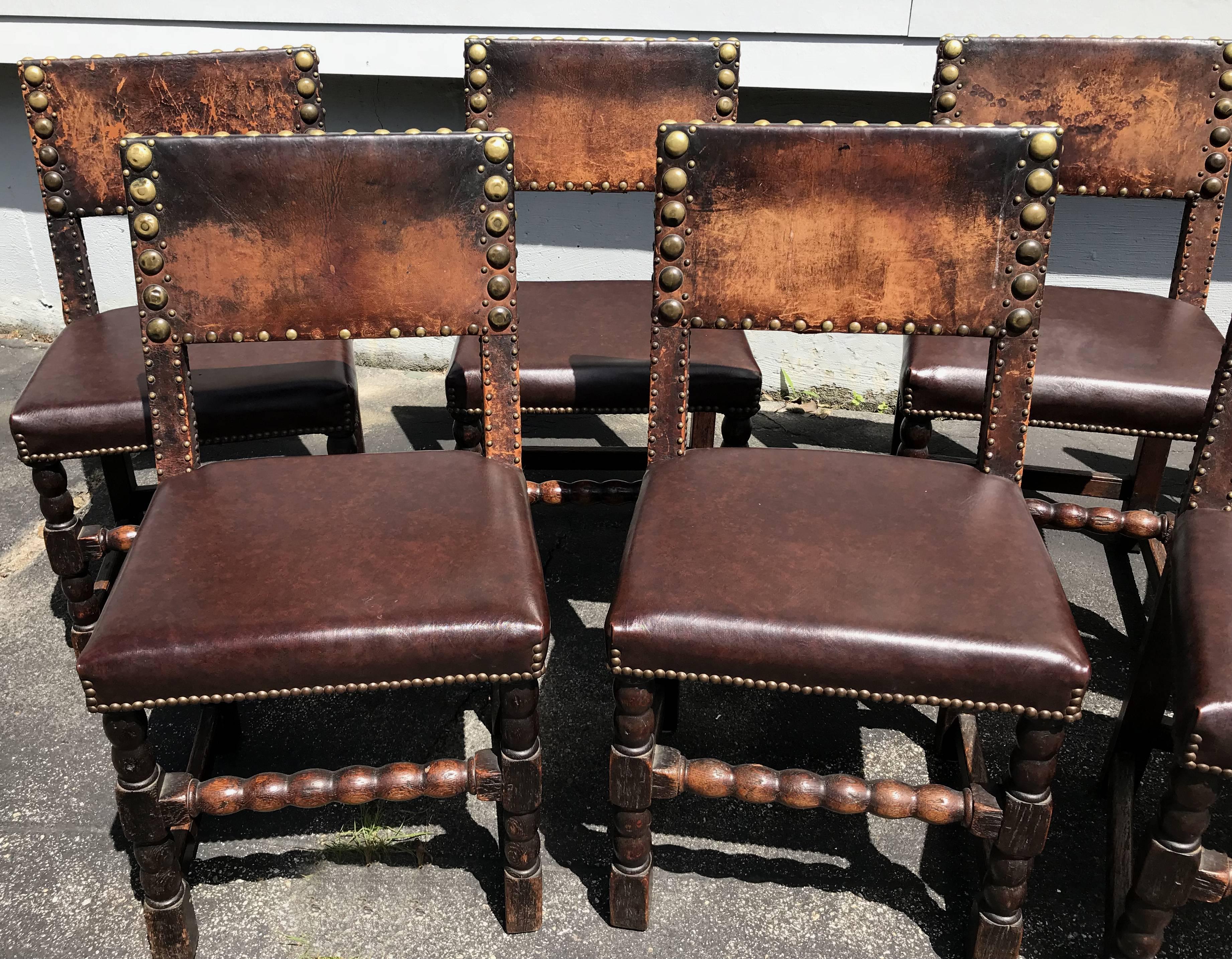 A great set of nine oak dining chairs with leather backs, adorned with bold brass nail upholstery trim. European in origin, dating to the late 17th or early 18th century, in good overall condition, with varying conditions of leather seat back wear