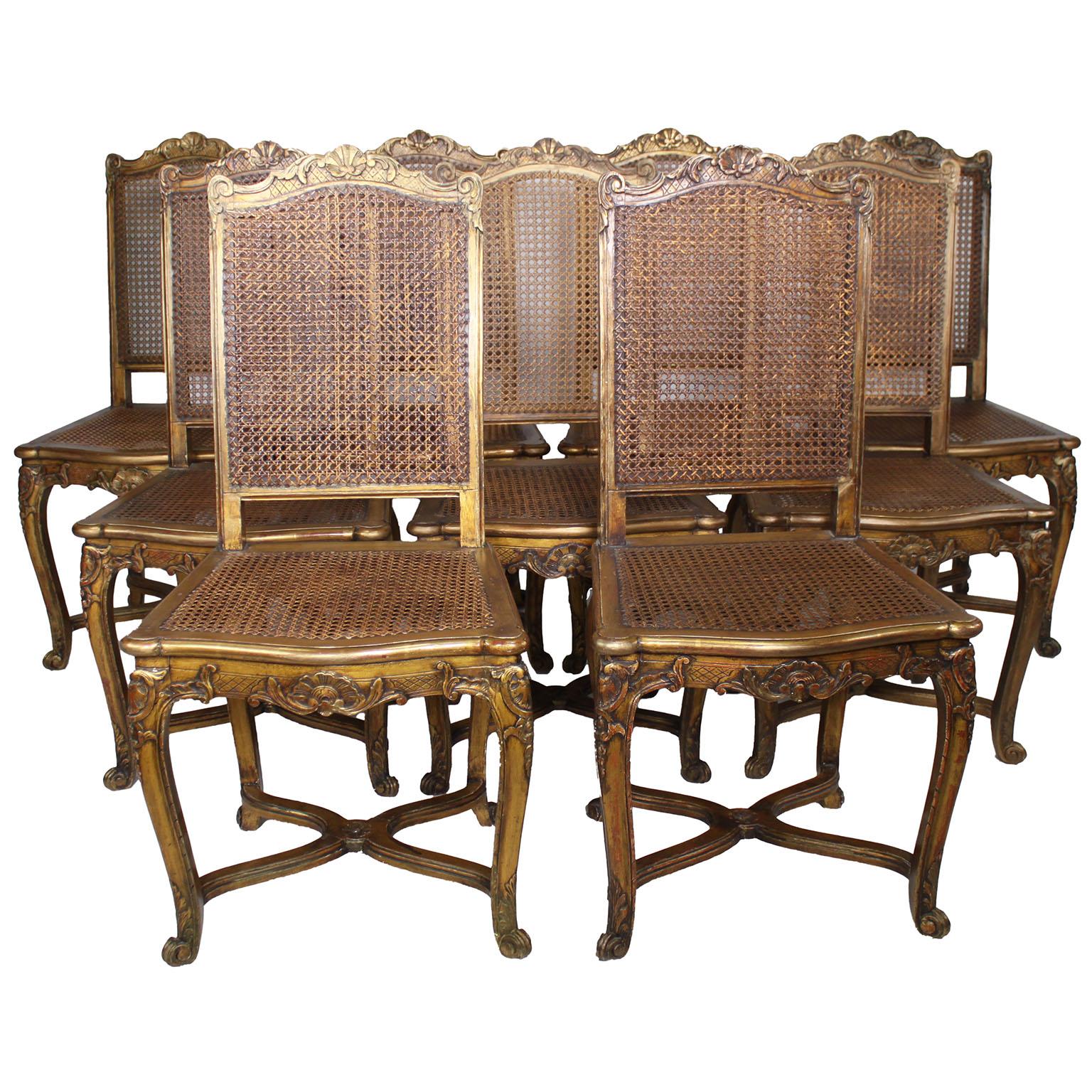 A Charming Set of Nine French 19th-20th Century Louis XV Style Gildwood Carved Opera-Concert Side Chairs. The delicately carved frames feature intricate motifs including seashells, scrolls, acanthus leaves, and flowers, elegantly supported by four