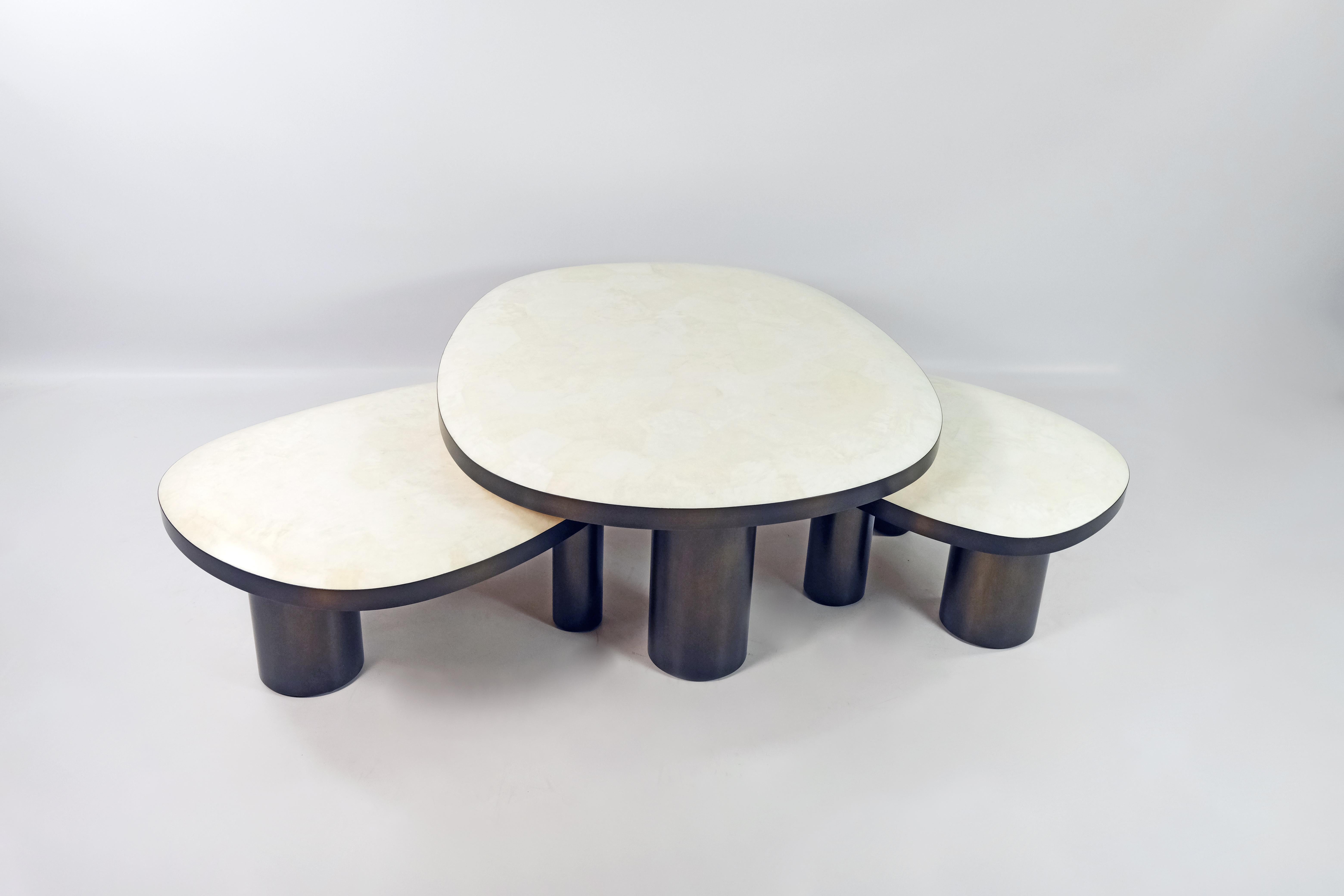 L'ensemble de 3 tables basses ovoïdes est constitué d'un plateau en marqueterie de cristal de roche blanc.
Les bords du plateau sont en laiton brossé bronzé.
Chaque table a trois pieds cylindriques en bois patiné.

Le dessus des tables est
