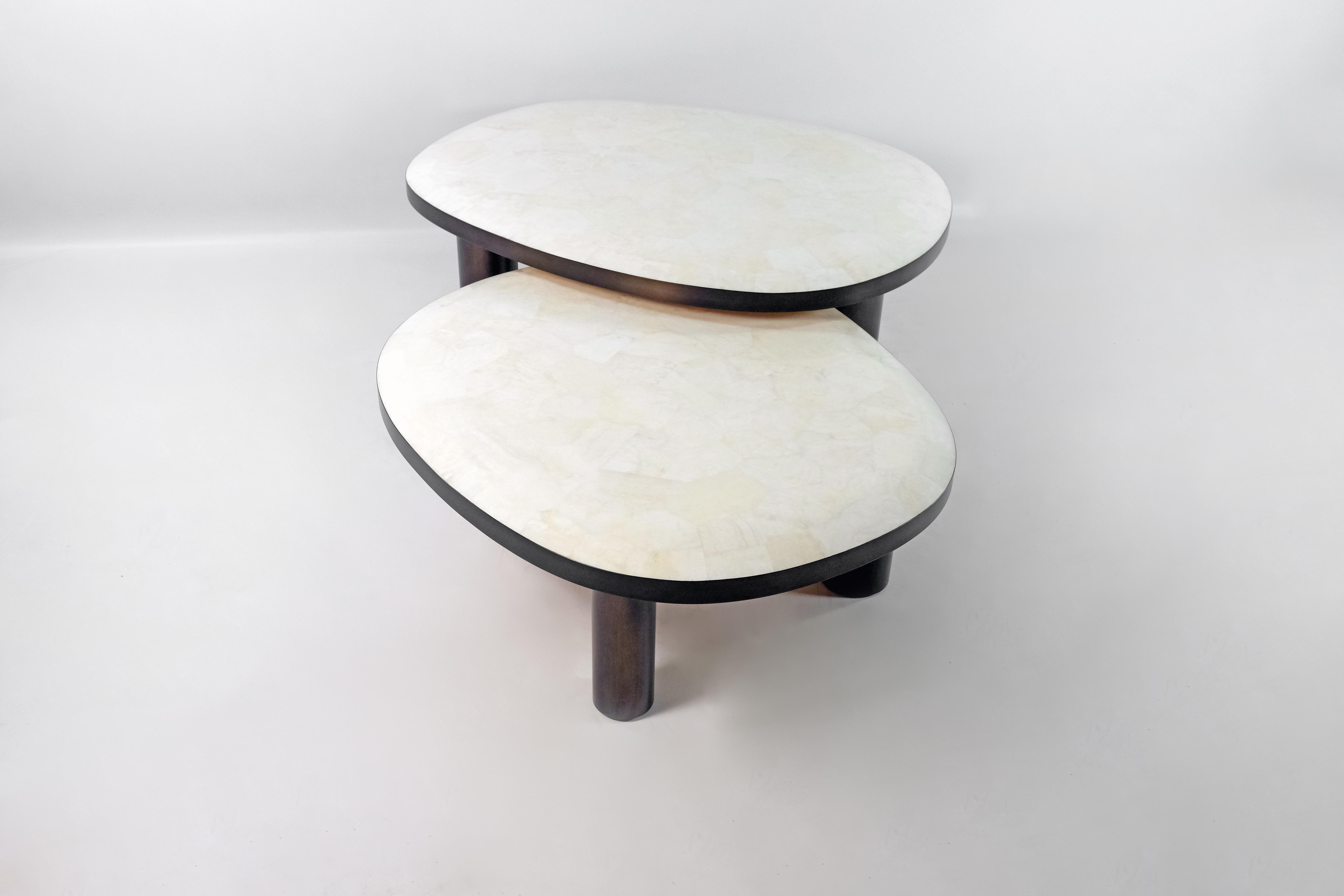 L'ensemble de 2 tables basses ovoïdes est constitué d'un plateau en marqueterie de cristal de roche blanc.
Les bords du plateau sont en laiton brossé bronzé.
Chaque table a trois pieds cylindriques en bois patiné.

Le dessus des tables est